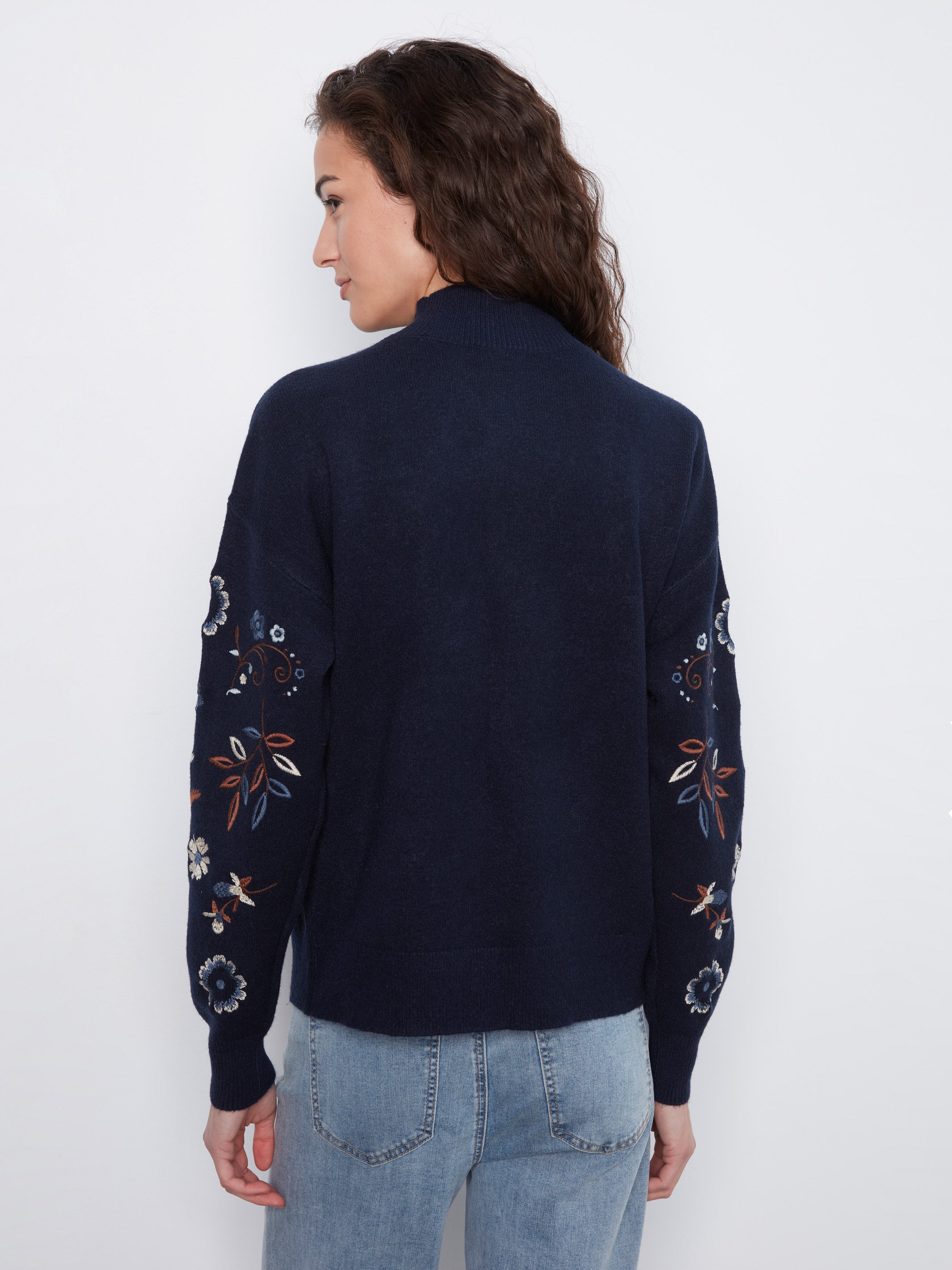 Back view of a navy blue sweater with floral embroidery on sleeves worn with light blue denim jeans.