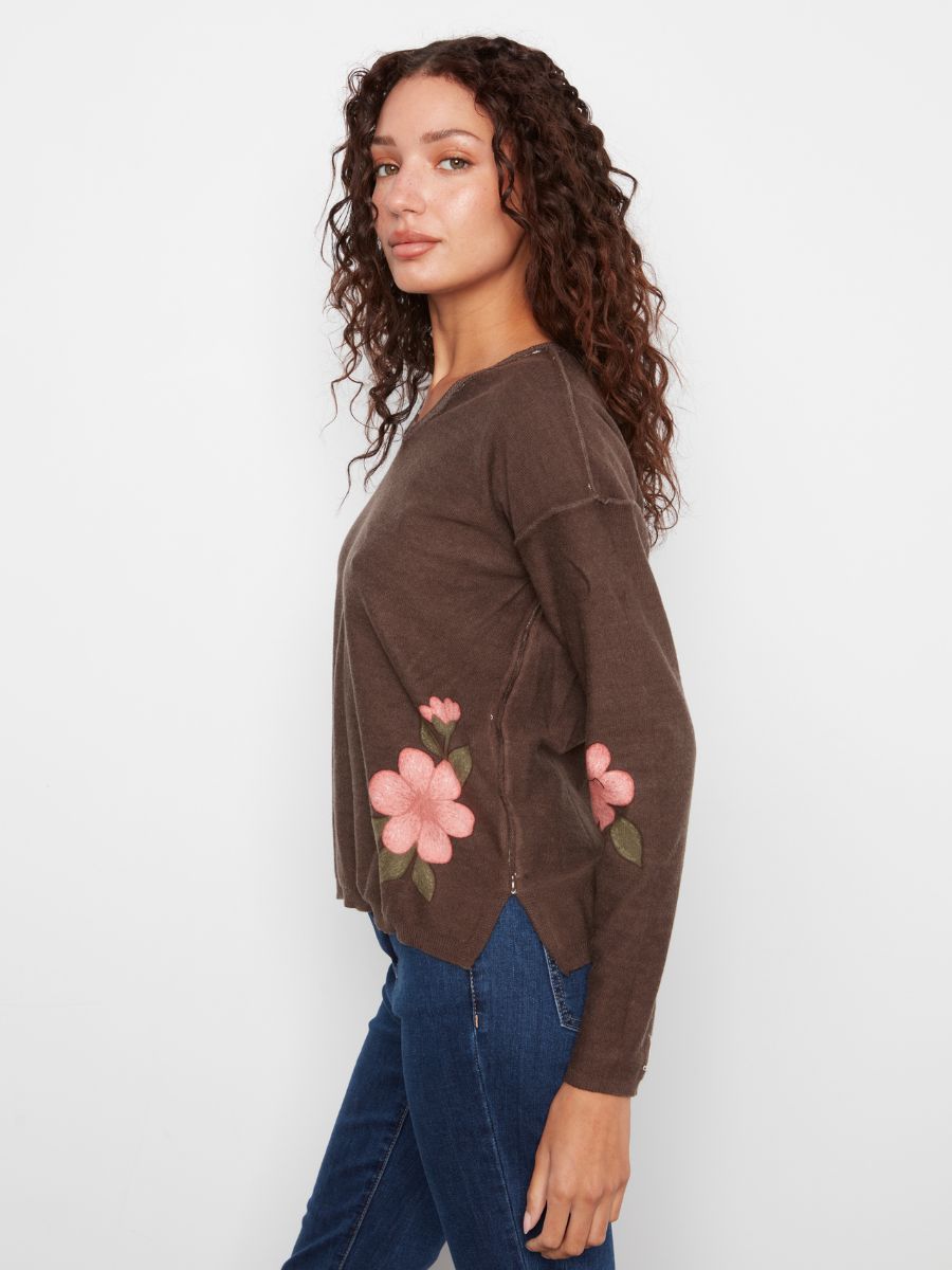 Side view of a brown long-sleeve sweater with pink floral embroidery paired with blue denim jeans.