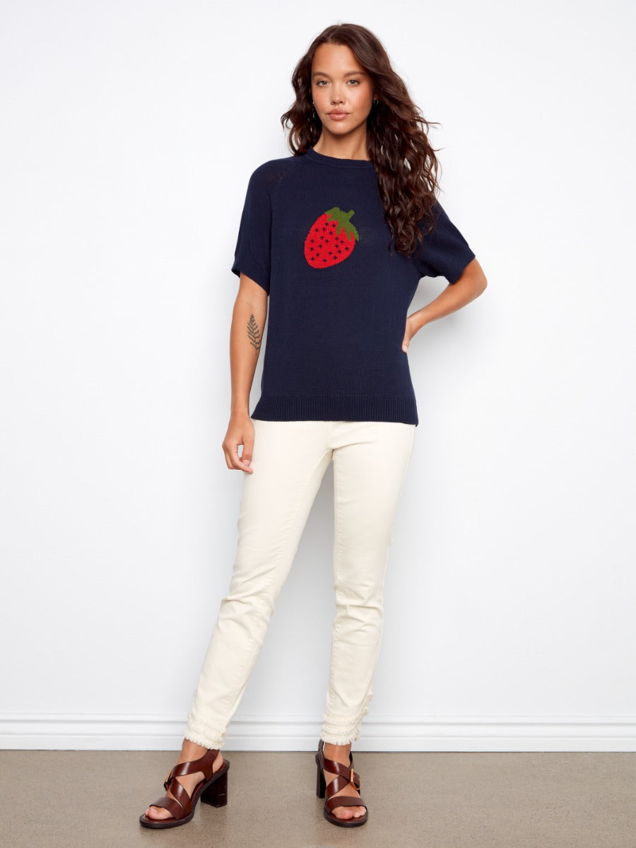 Charlie B Strawberry Short Sleeve Crochet Sweater in navy with strawberry design, styled with cream pants and brown sandals