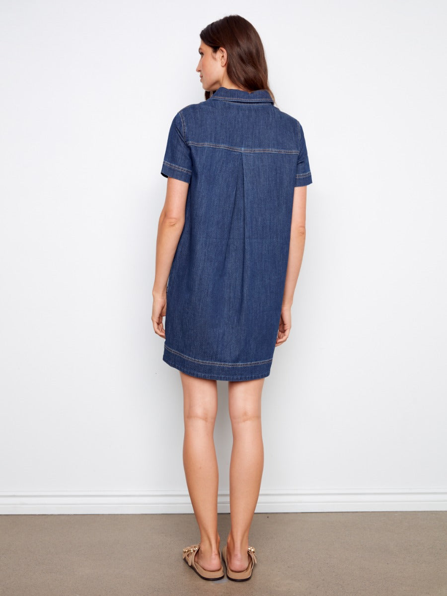 Back view of a person wearing a dark blue denim short-sleeve dress with a collar, standing on a neutral floor.