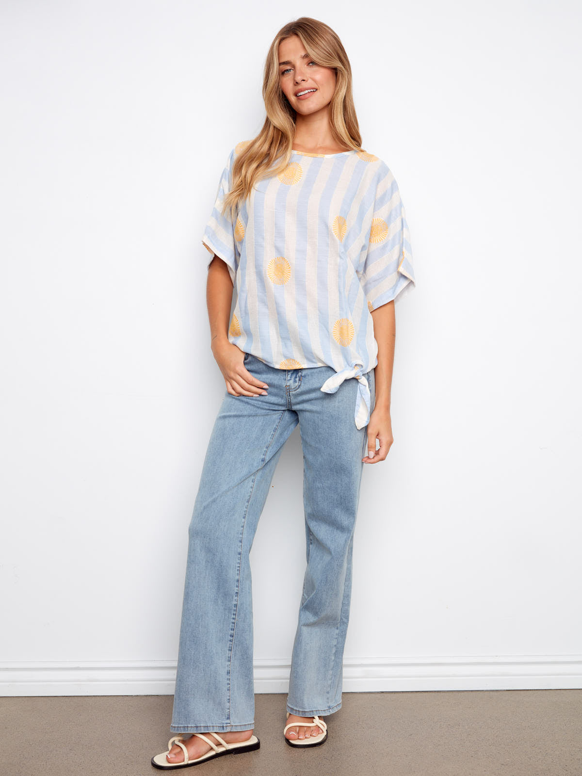 Charlie B Sunrise Striped Tie Short Sleeve Top in pastel blue and white stripes with yellow sun accents, paired with jeans.