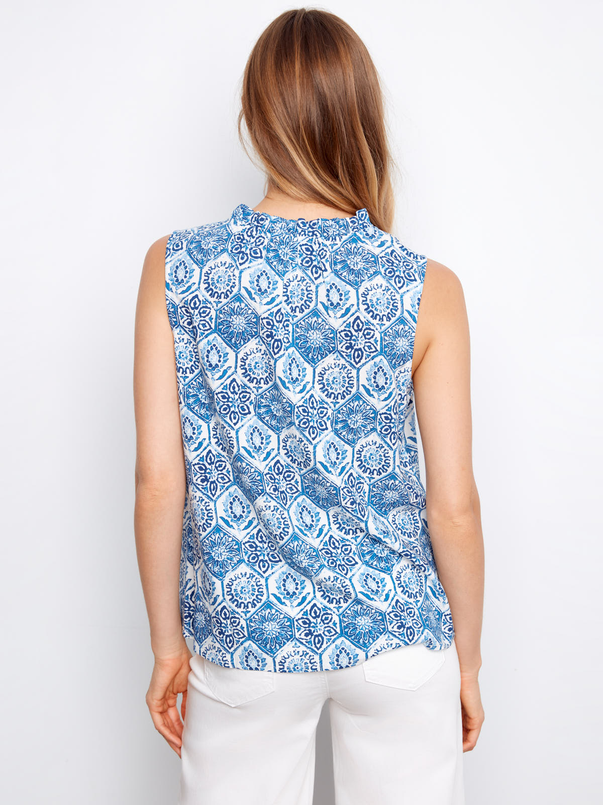 Back view of a sleeveless blue patterned Charlie B Layered or Not Ruffle Top paired with white pants