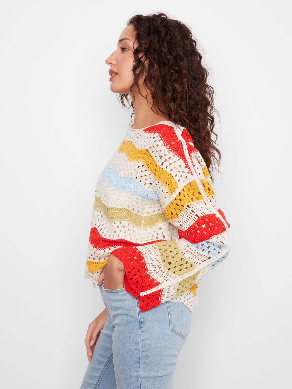 Model in colorful crochet top with red, yellow, blue, and cream stripes styled with light denim jeans, Charlie B Solstice Crochet Crew Top