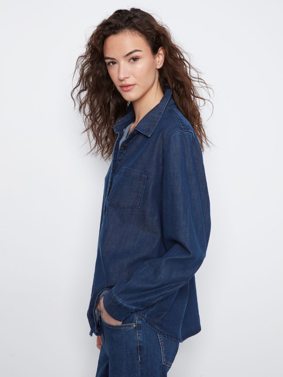 Profile view of a person with long curly hair wearing a dark indigo denim shirt and matching jeans against a white background.