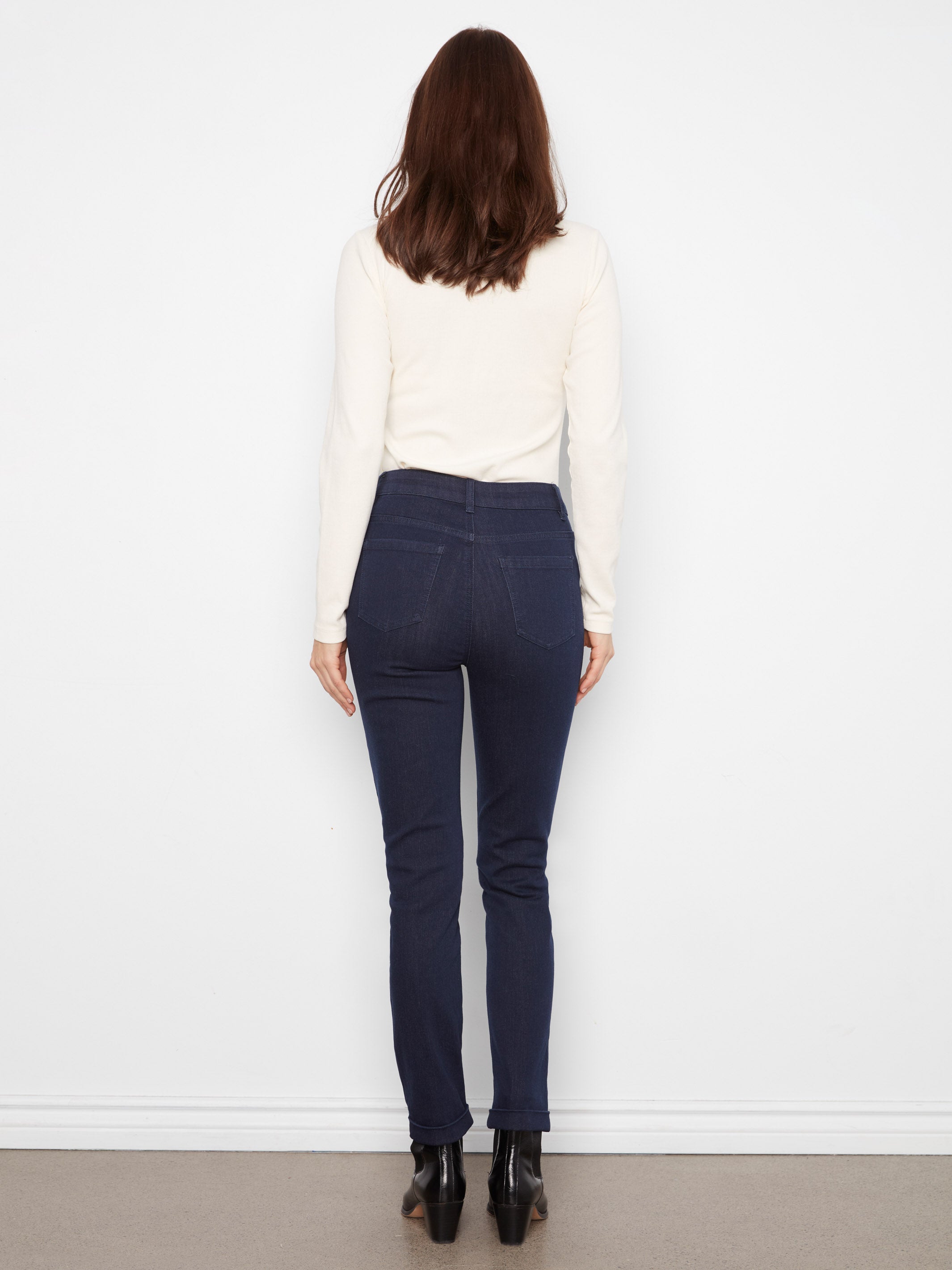 Back view of a figure in dark denim pants, a cream long-sleeve top, and black ankle boots against a white background.