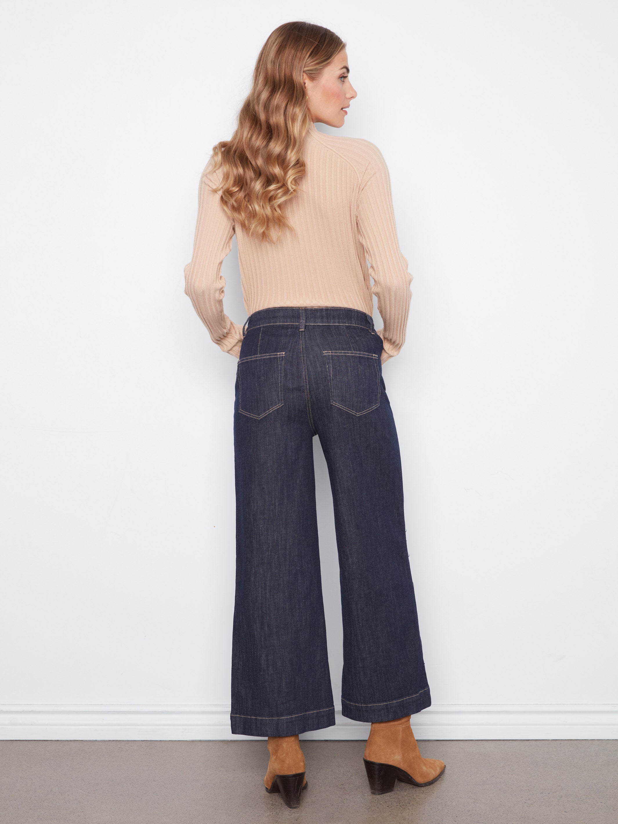 Back view of a figure in a beige ribbed sweater, wide-leg dark denim jeans, and tan suede ankle boots.