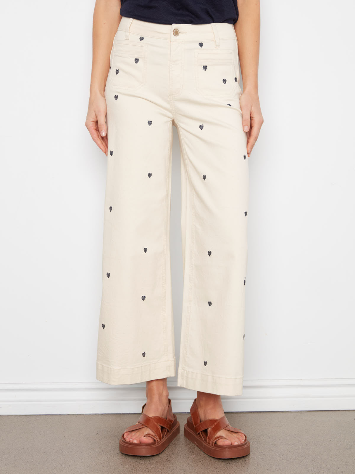 Charlie B Hearts Double Trouble Denim Jean in natural color with black heart prints paired with brown sandals.