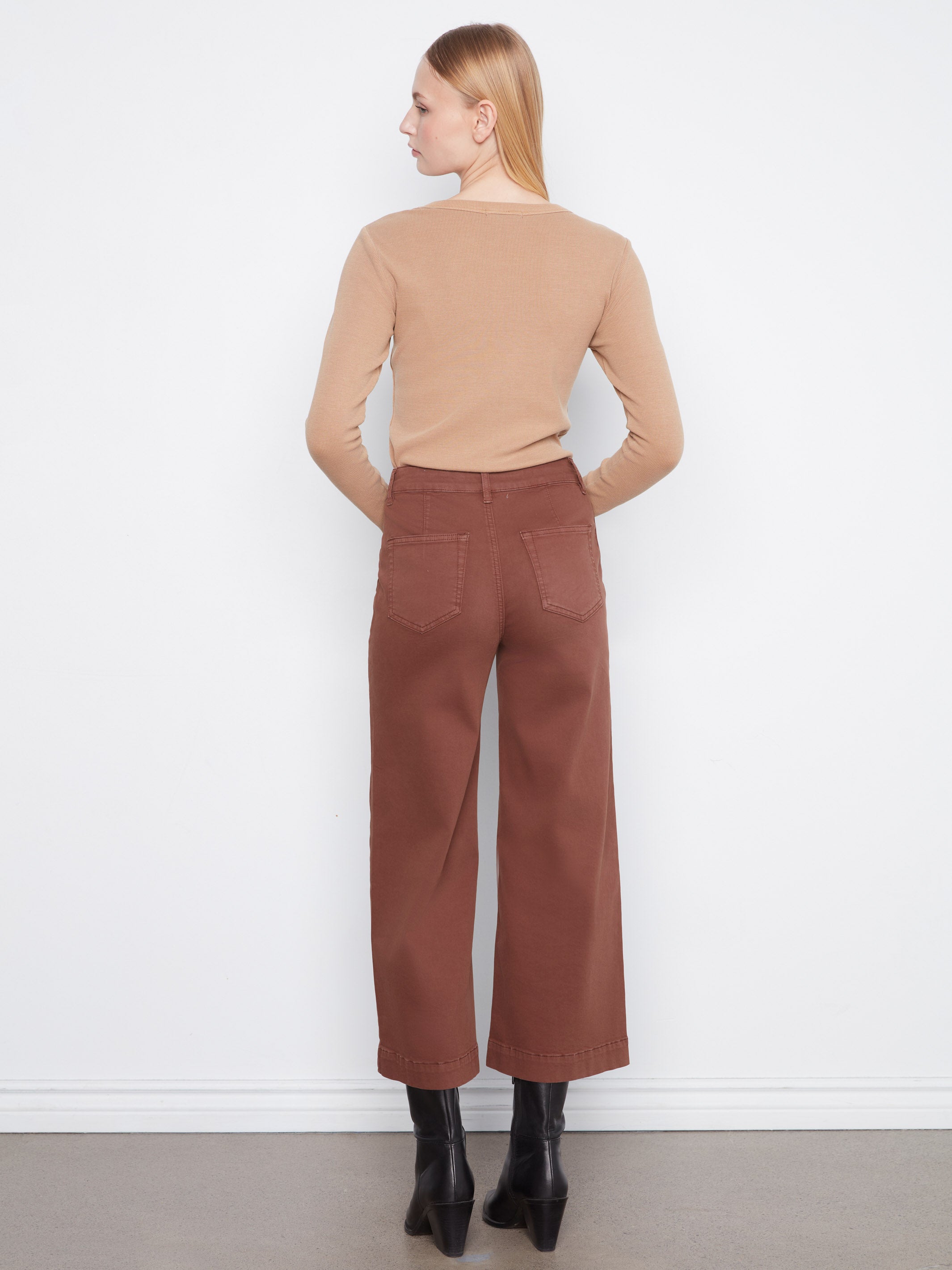 Back view of a figure in a beige long-sleeve top and wide-leg brown pants with black heeled boots.