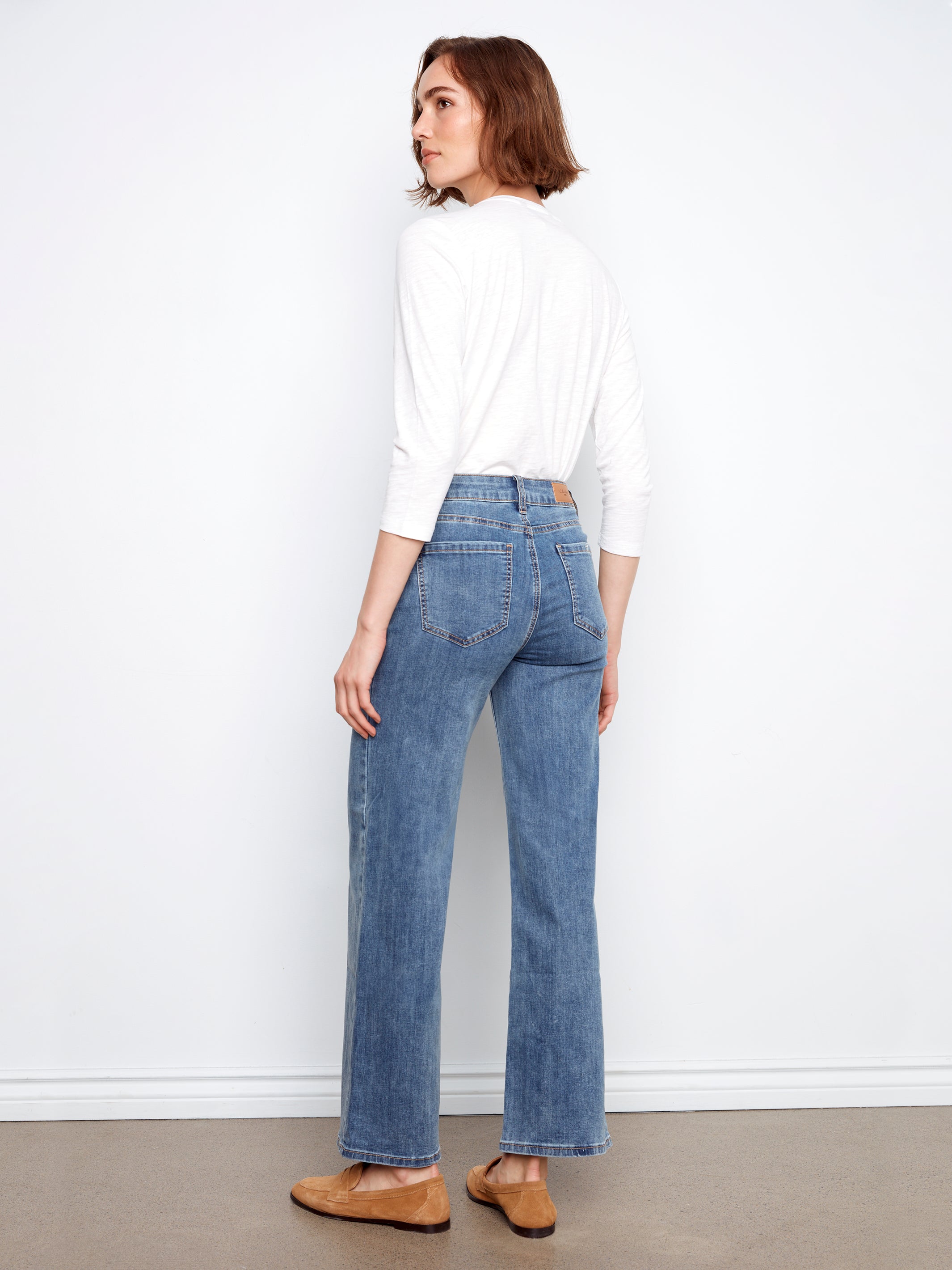 Model seen from back wearing Charlie B Chloe Wide Leg Denim Jeans in medium blue wash by Charlie B with white top and brown shoes