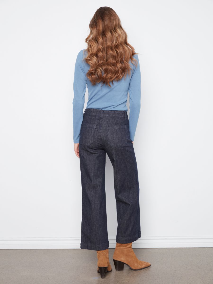 Back view of a figure wearing a light blue long-sleeve top, dark denim wide-leg pants, and tan ankle boots.