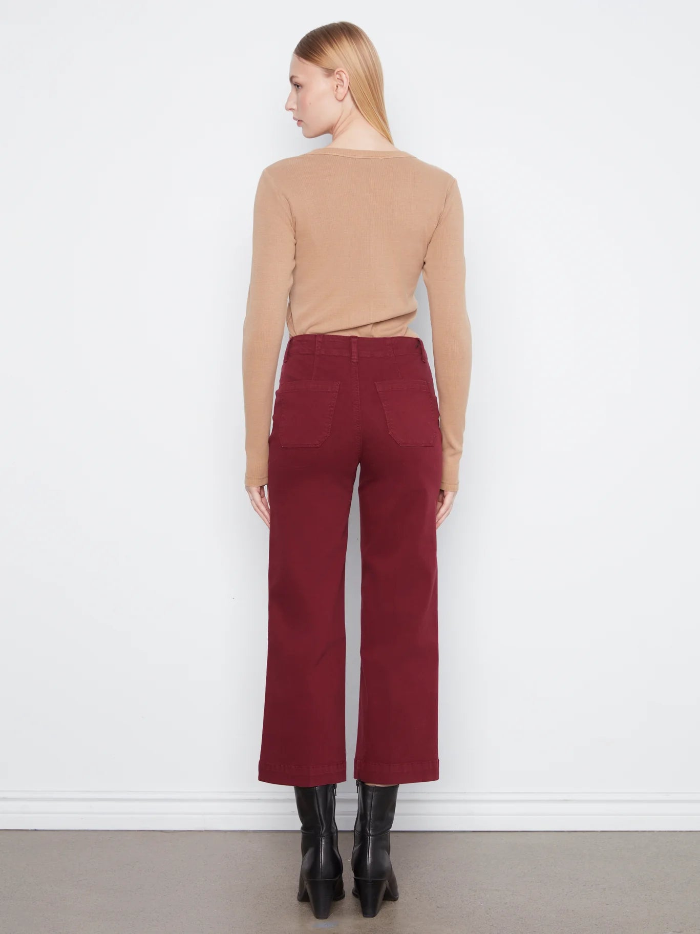 Rear view of a slim figure in a beige long-sleeve top and high-waisted wide-leg maroon pants with black ankle boots.
