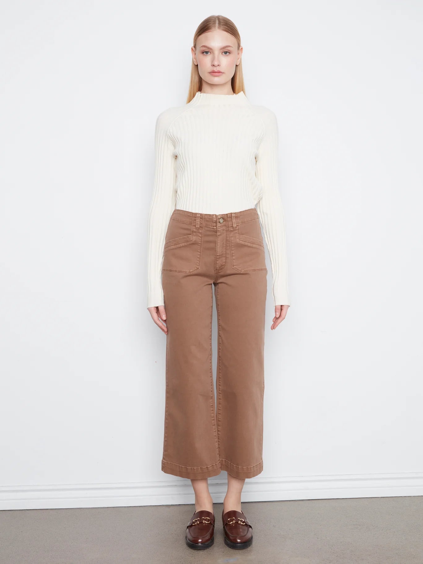 White ribbed long-sleeve sweater paired with high-waisted wide-leg brown denim pants and brown loafers.