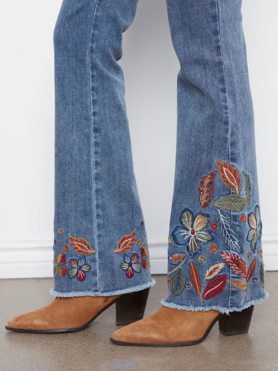 Blue denim jeans with colorful floral embroidery near the frayed hem paired with brown suede pointed-toe boots.