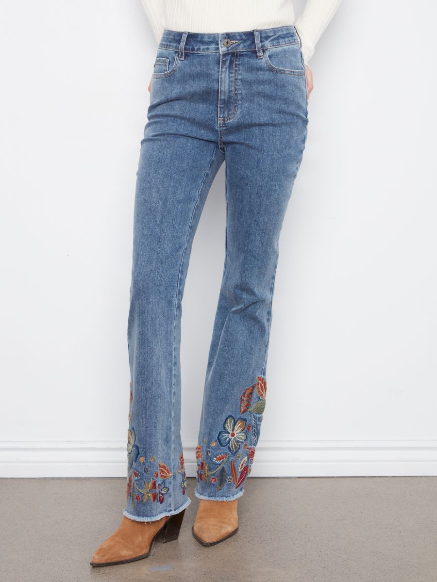 Blue denim jeans with floral embroidery along the lower legs paired with tan pointed-toe boots.