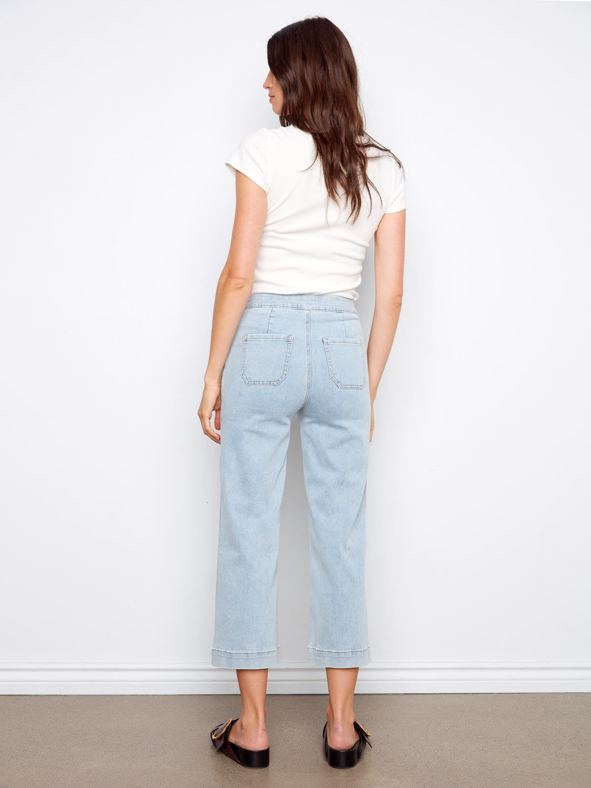 Rear view of light wash denim pants in Charlie B Triple Threat 26” Denim Capris by Charlie B paired with white short sleeve top