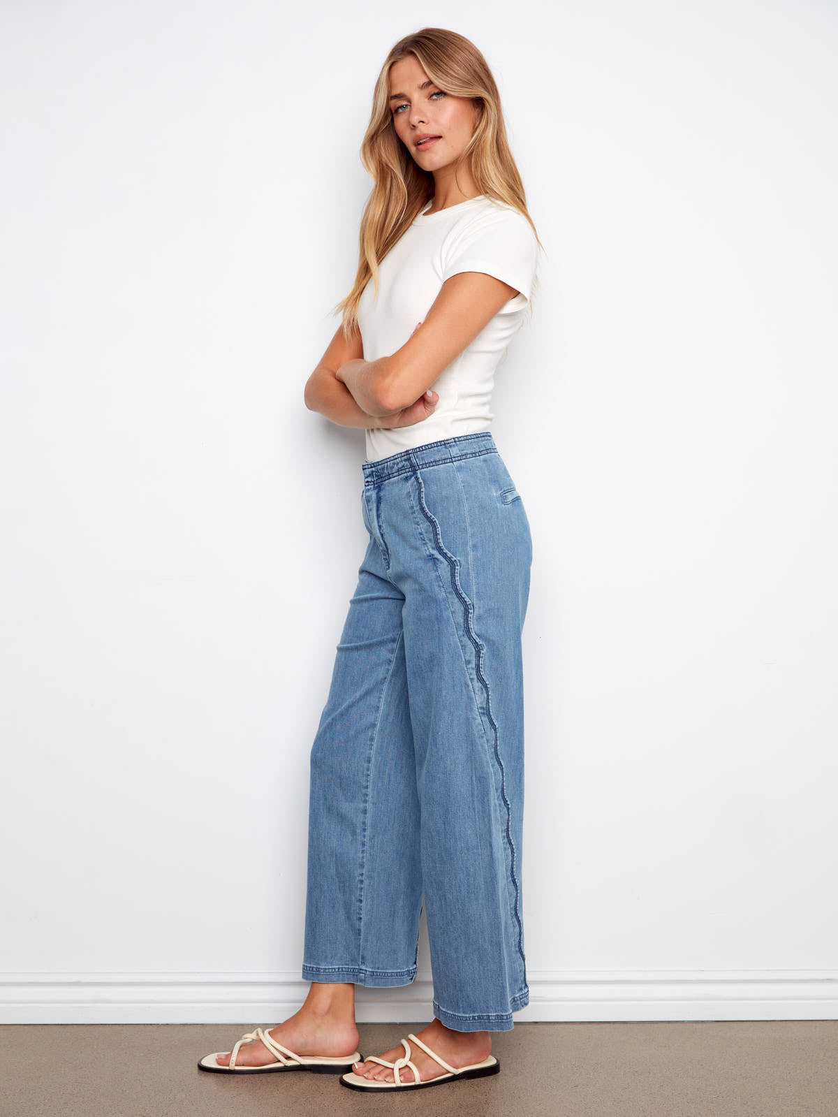 Charlie B Scallop Wave 27” Denim Pant in light blue with scalloped side detail, styled with a white top and sandals