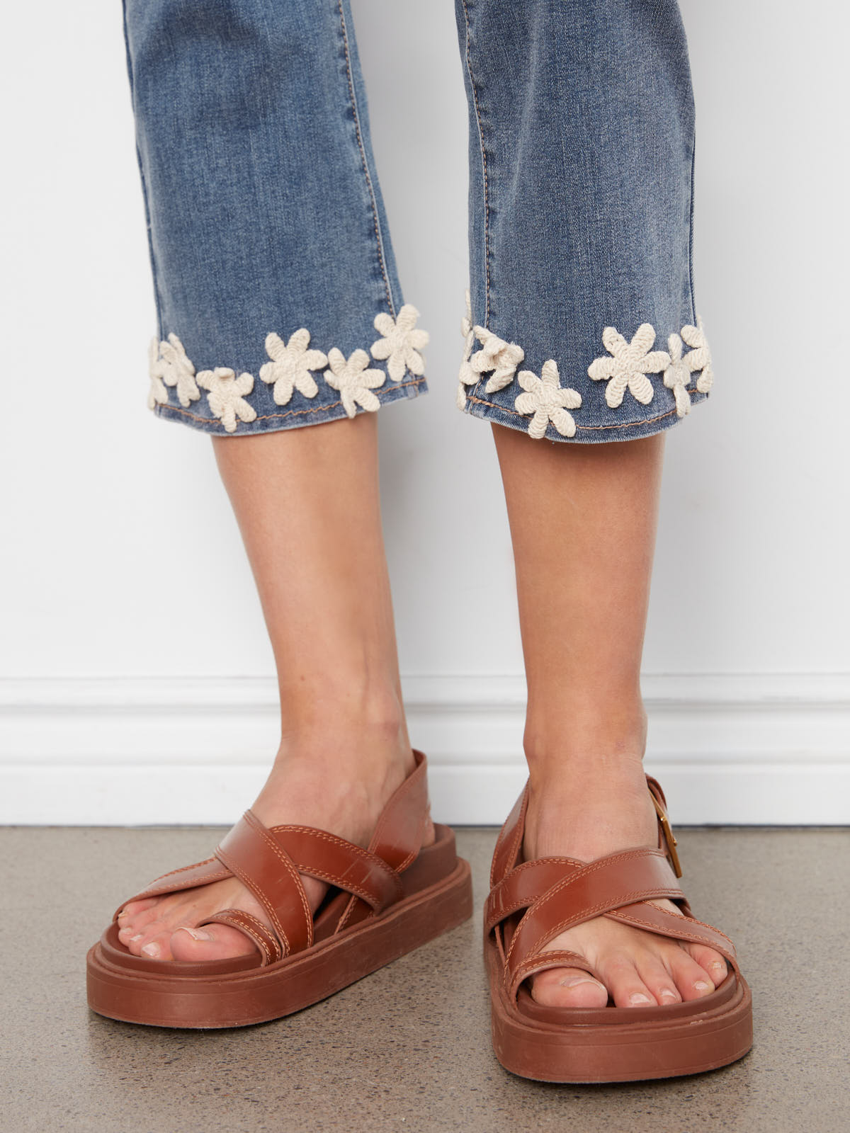 Close-up of Charlie B Crochet Flower Hem Denim Capris paired with brown leather platform sandals by Charlie B.