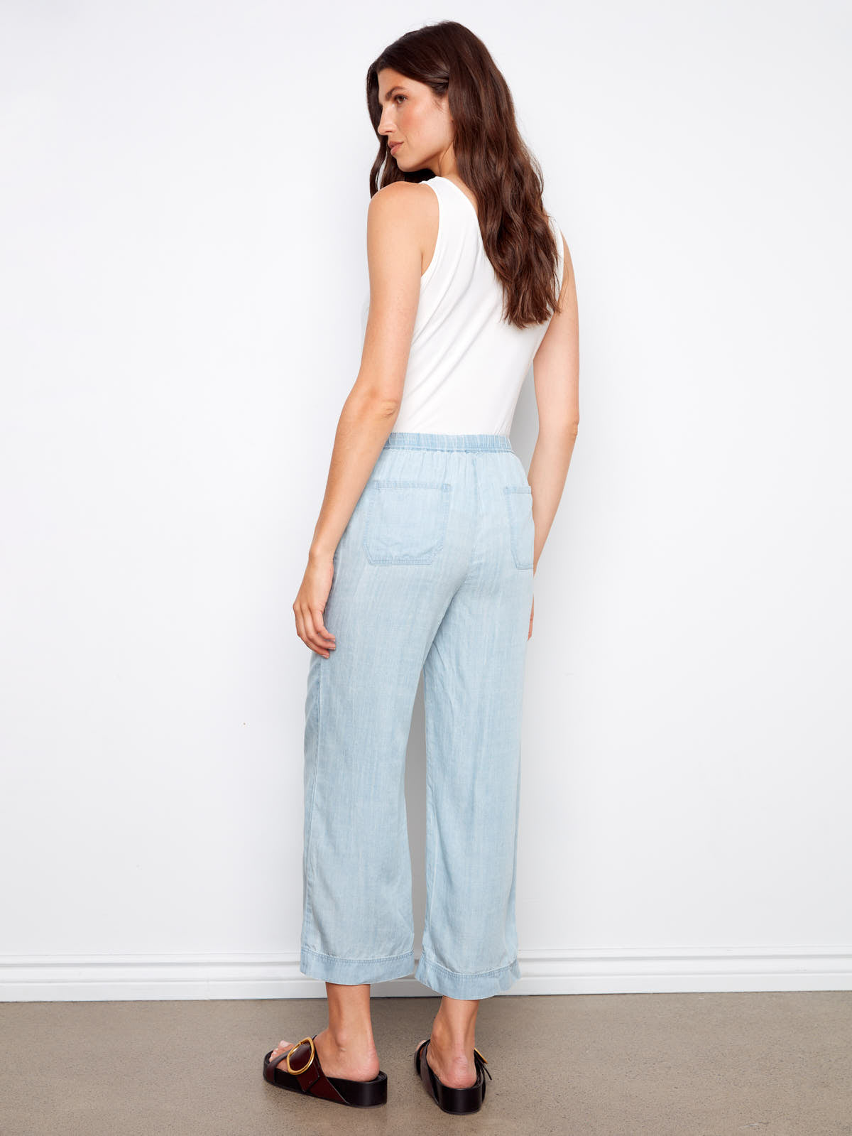 Charlie B Travel 4 Tencel Cropped Pant in light blue denim styled with a white sleeveless top and black slide sandals