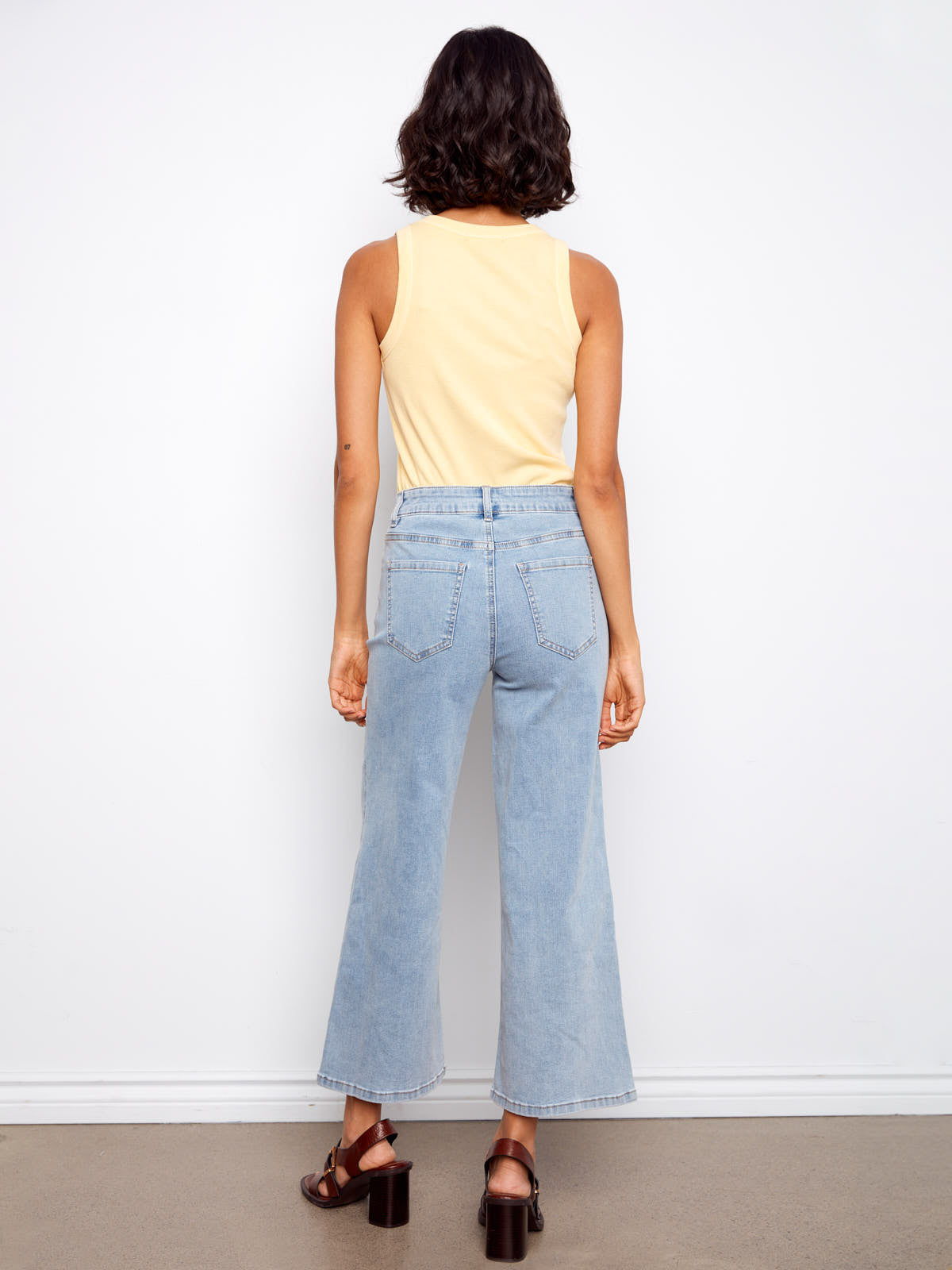 Back view of light wash denim jeans styled with a sleeveless top and sandals featuring Charlie B Daisy Beads Embroidered Denim Jeans