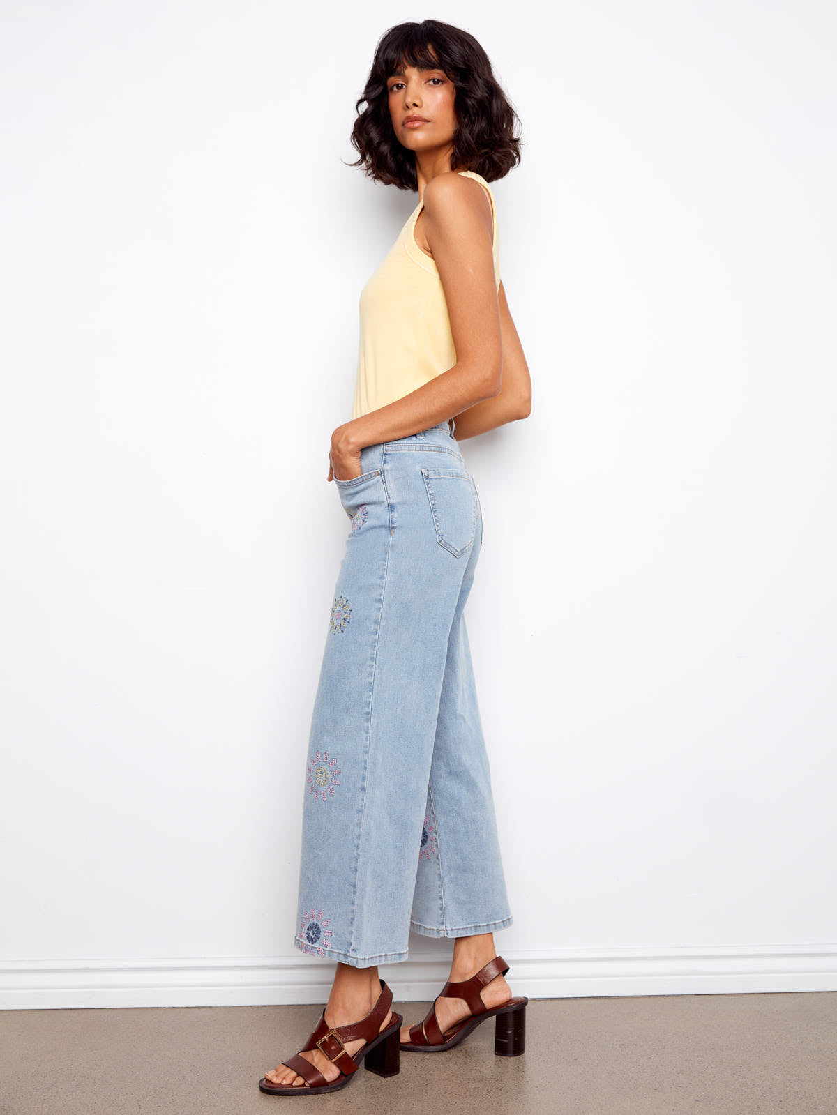 Slim figure wearing light blue Charlie B Daisy Beads Embroidered Denim Jeans with floral bead details and brown heeled sandals