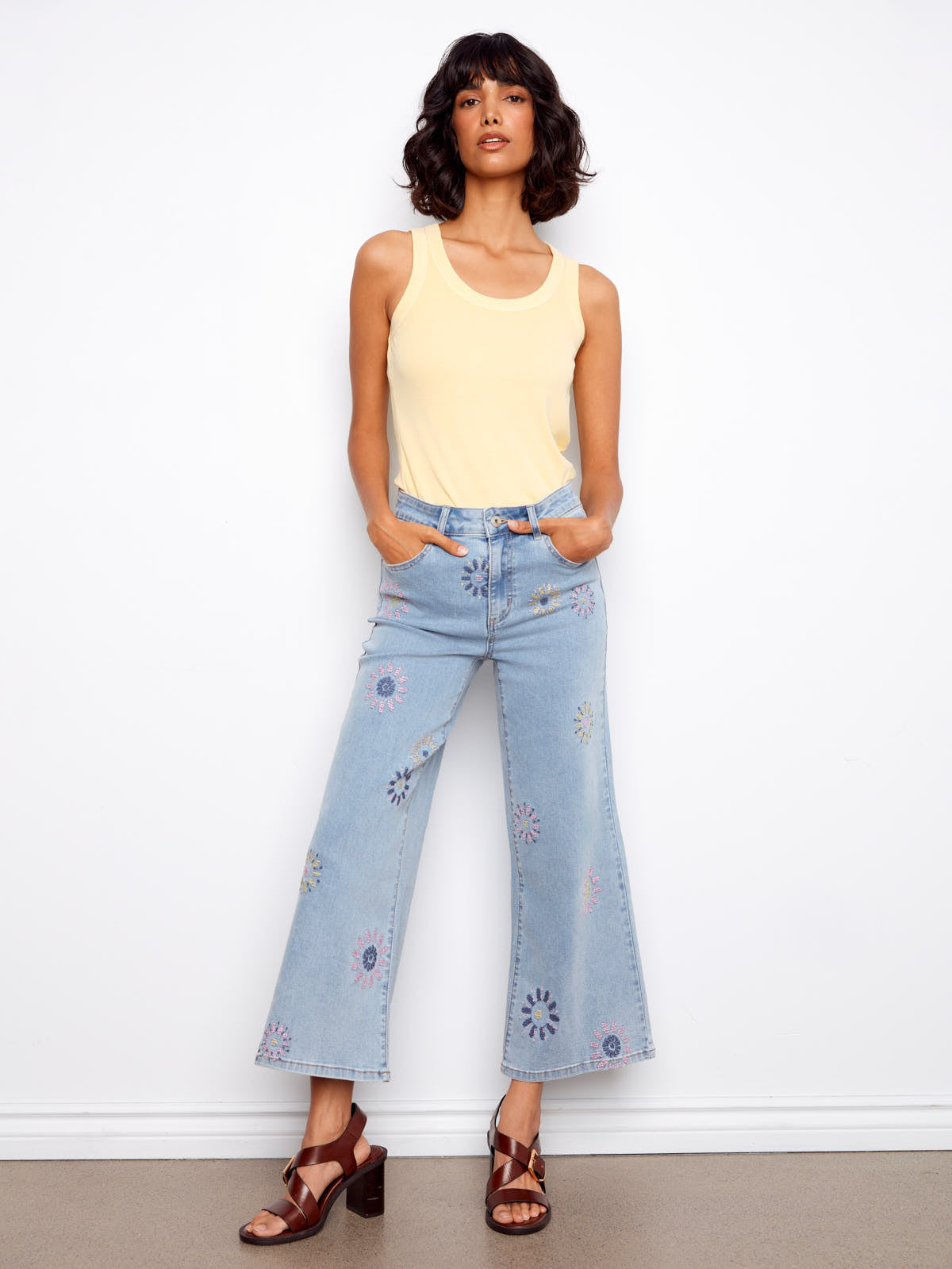 Light wash floral embroidered Charlie B Daisy Beads Embroidered Denim Jeans styled with a yellow tank top and brown heels.