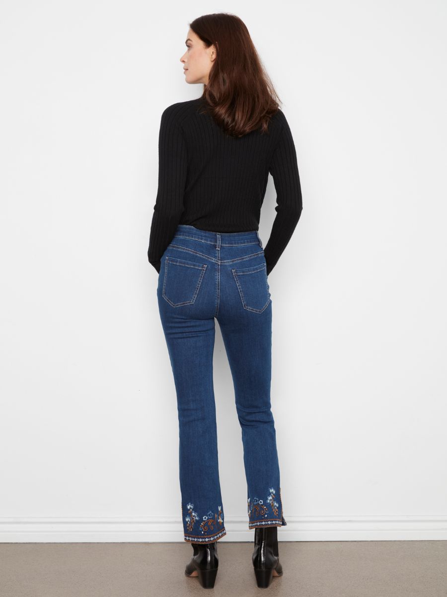 Rear view of a figure in blue denim jeans with floral embroidery at the hem and a black ribbed long-sleeve top