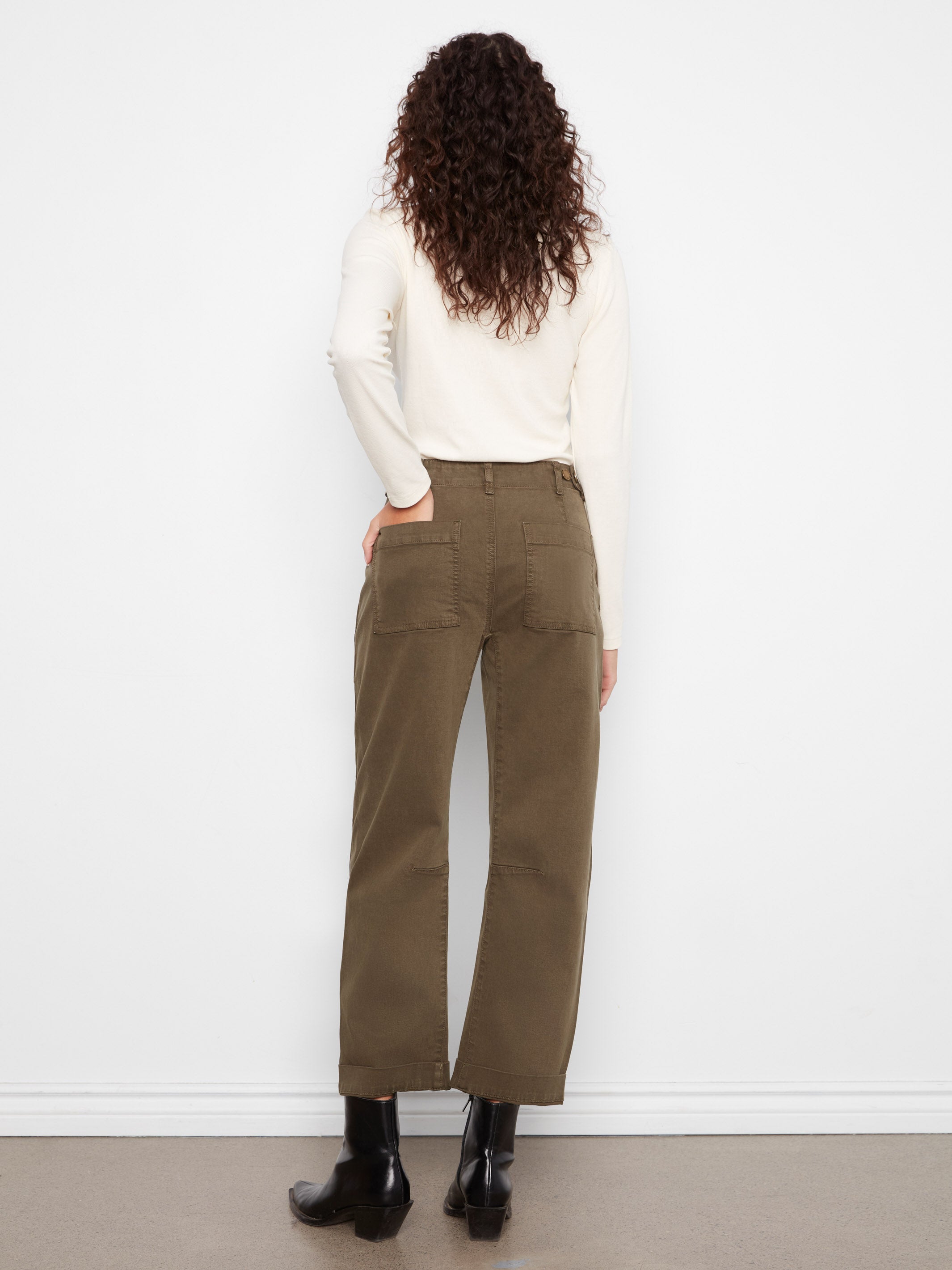 Back view of a figure in olive green wide-leg pants with patch pockets, a long-sleeve cream top, and black ankle boots.