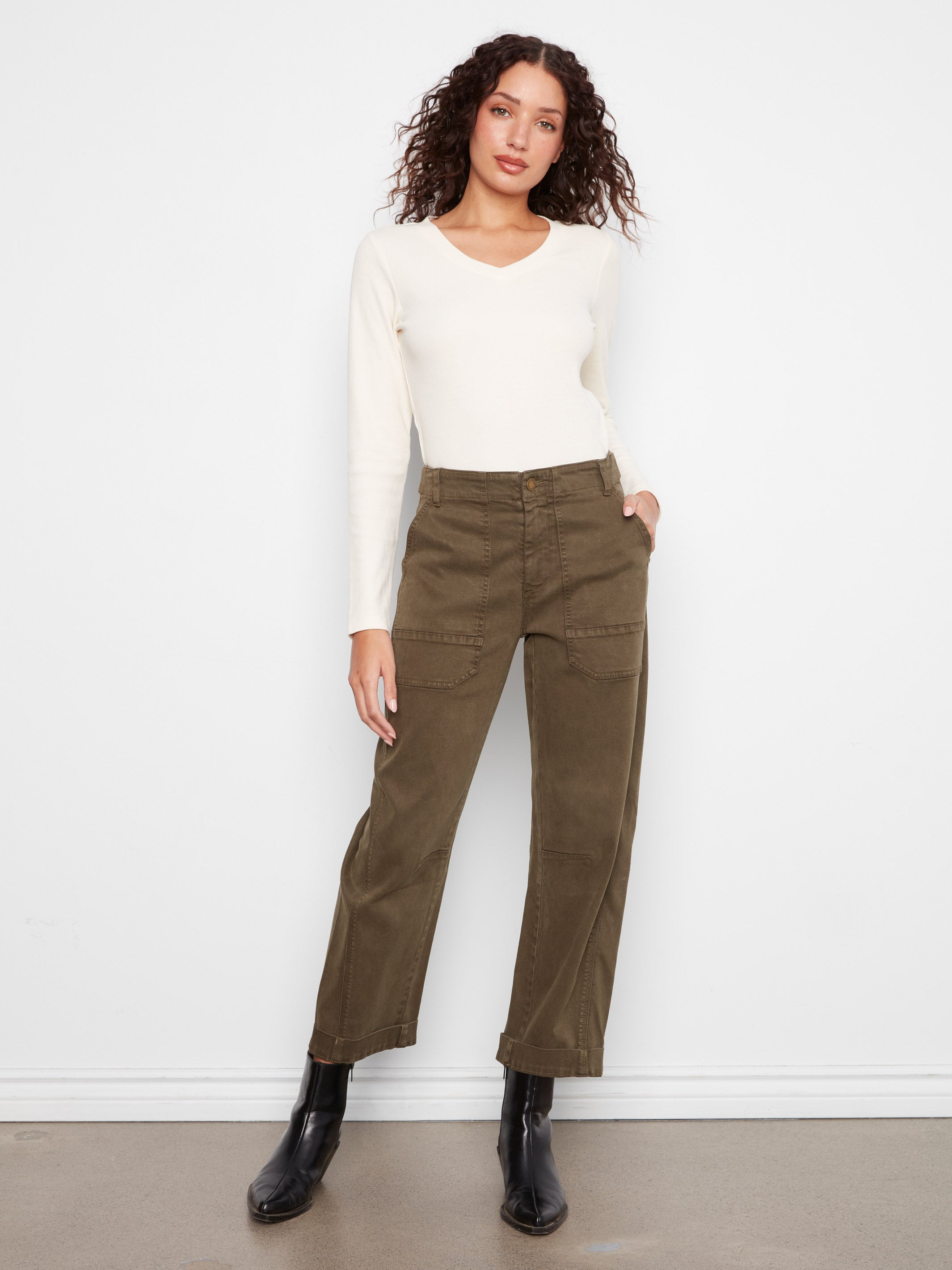 Model in white long-sleeve top, olive green pants with large front pockets, and black ankle boots against white background.