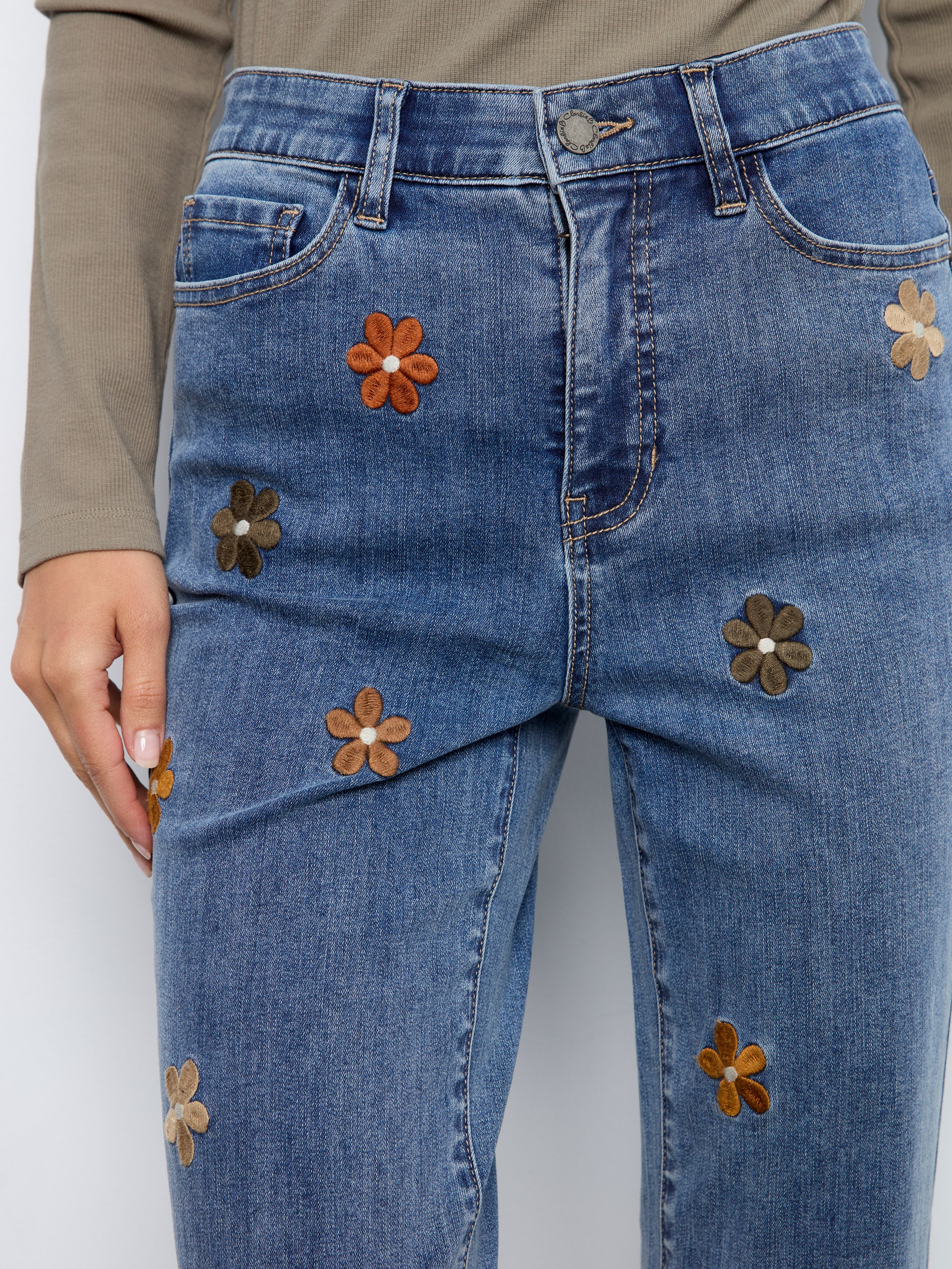 Close-up of blue denim jeans with embroidered brown and beige flower patterns on the front.