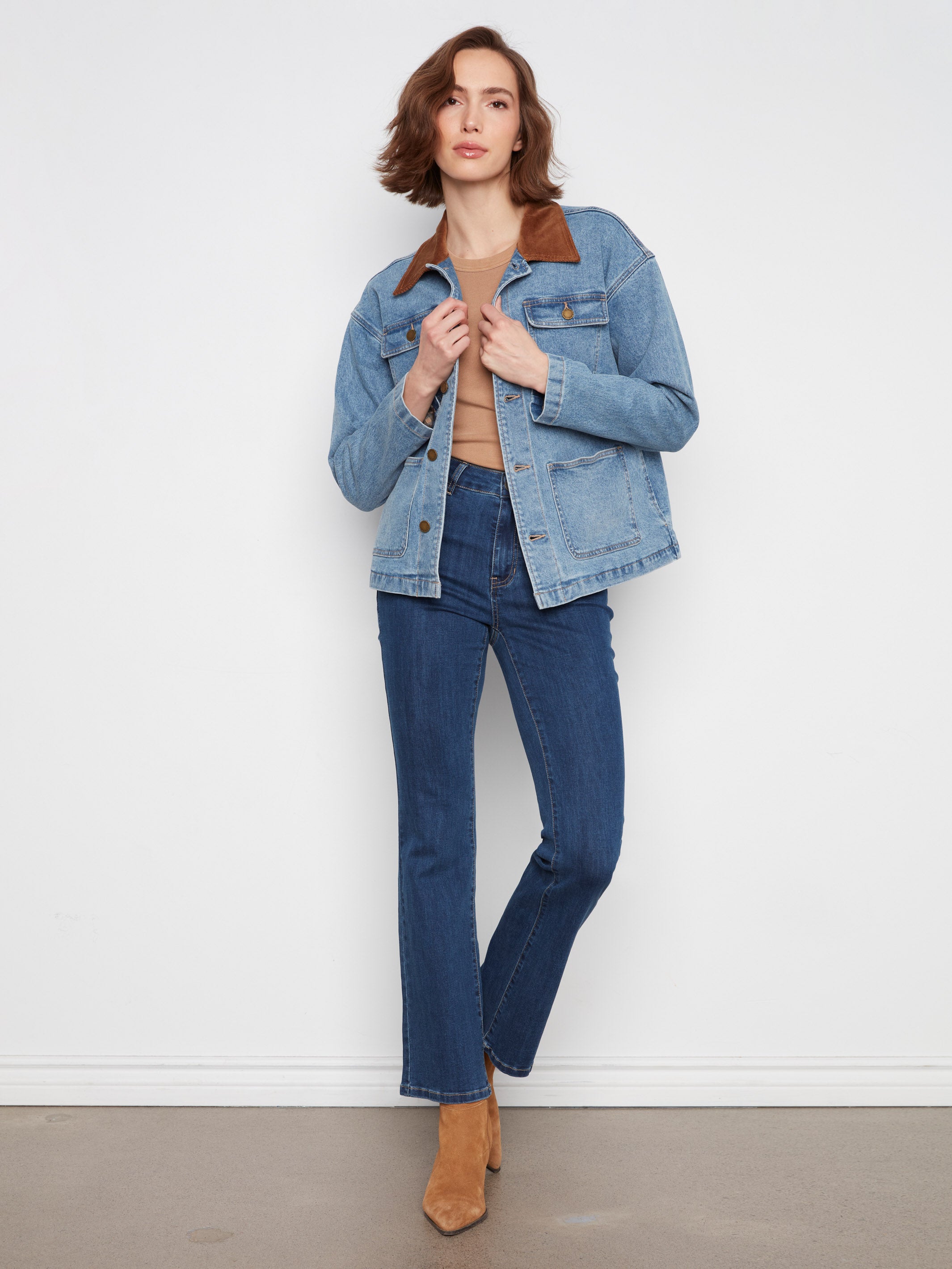 Light denim jacket with brown collar paired with dark blue jeans and tan suede boots on plain background
