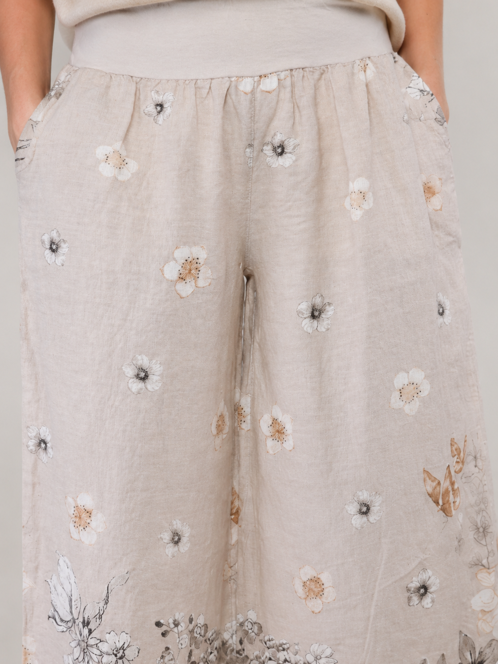 Beige lightweight linen trousers with an elastic waistband and scattered floral print in neutral tones.