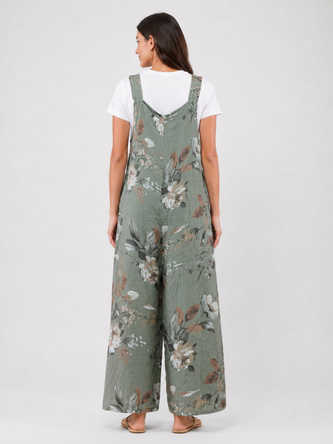 Back view of olive green floral wide-leg jumpsuit layered over a white short sleeve top with adjustable straps.