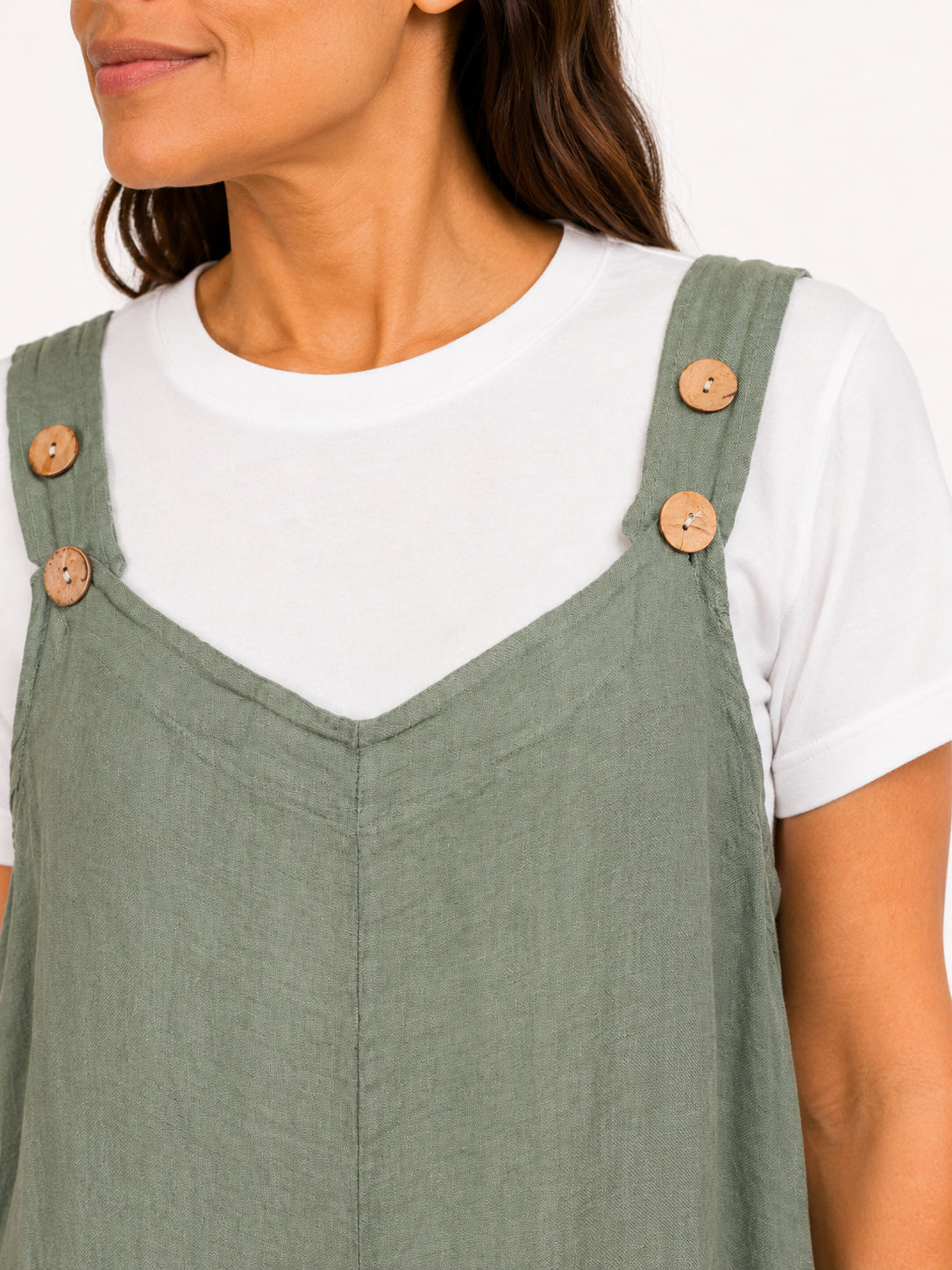 Close-up of olive green linen dress with wooden button straps over a white short sleeve shirt.