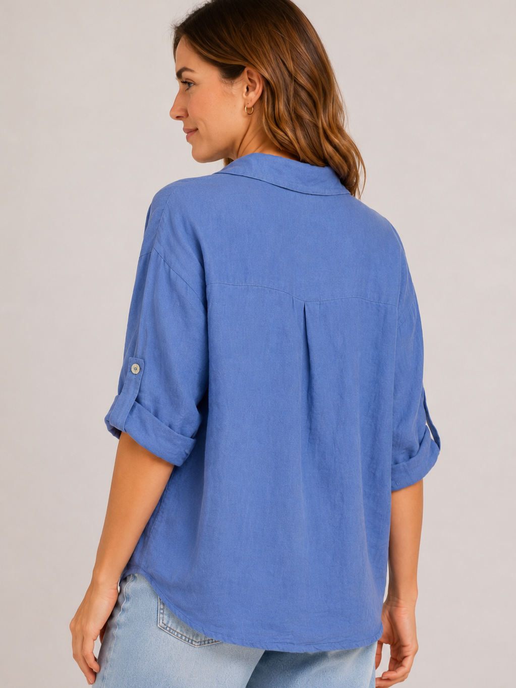 Back view of a blue denim long-sleeve shirt with rolled sleeves paired with light-wash denim jeans against a plain background.