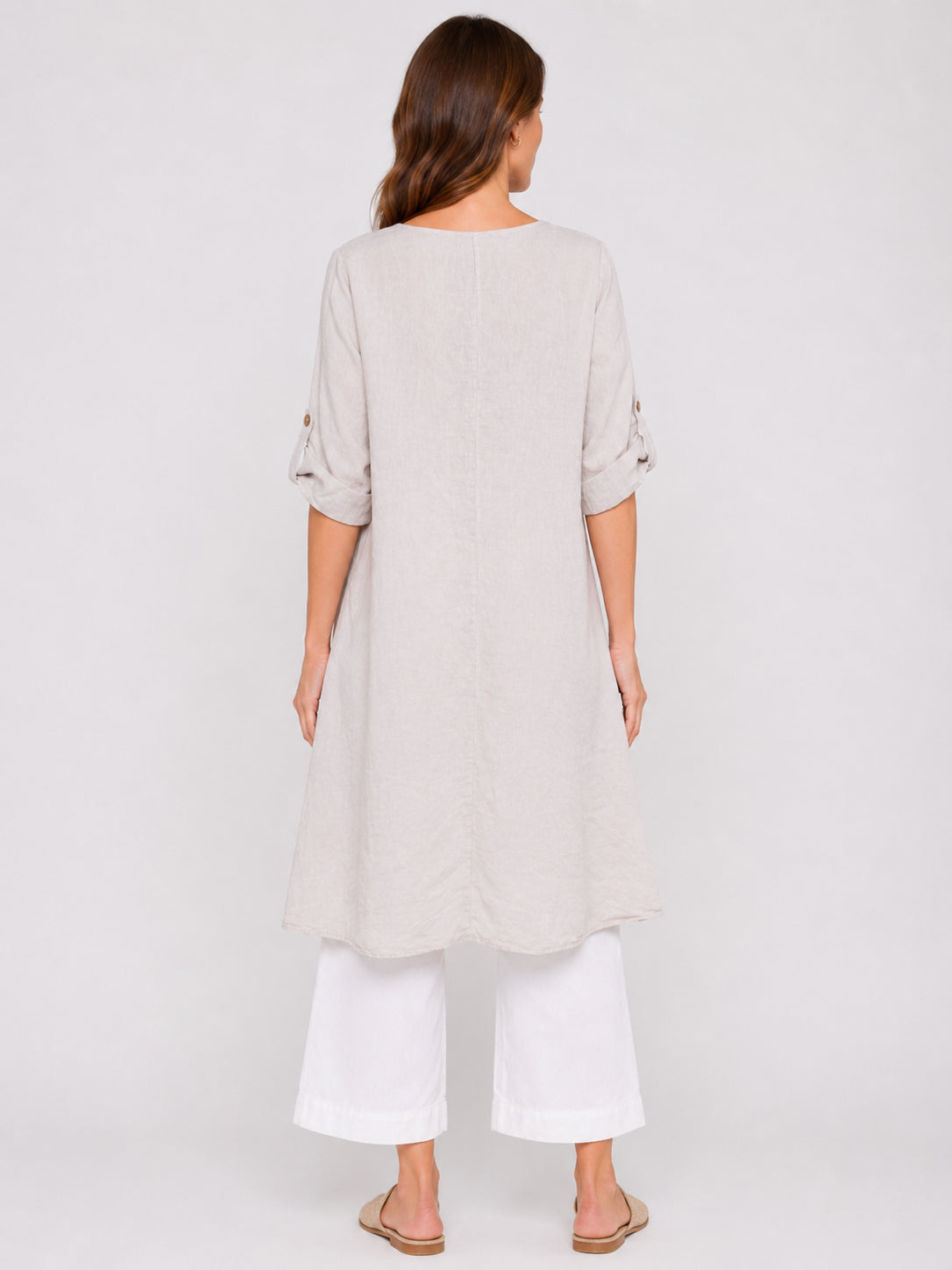 Beige long-sleeve linen tunic with buttoned rolled sleeves, paired with wide white cropped pants and sandals.