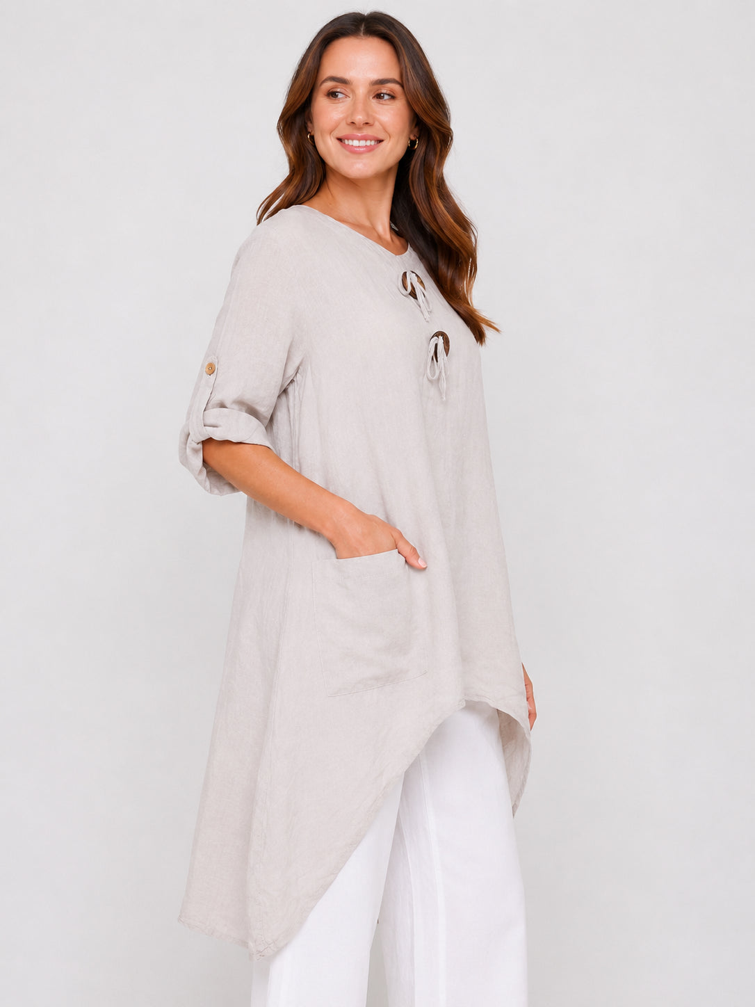 Light beige asymmetrical tunic top with roll-up sleeves and front pocket, styled with white pants.