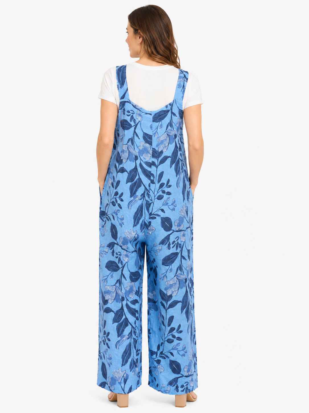 Back view of a blue floral patterned wide-leg jumpsuit worn over a white short-sleeve top on a plain background.