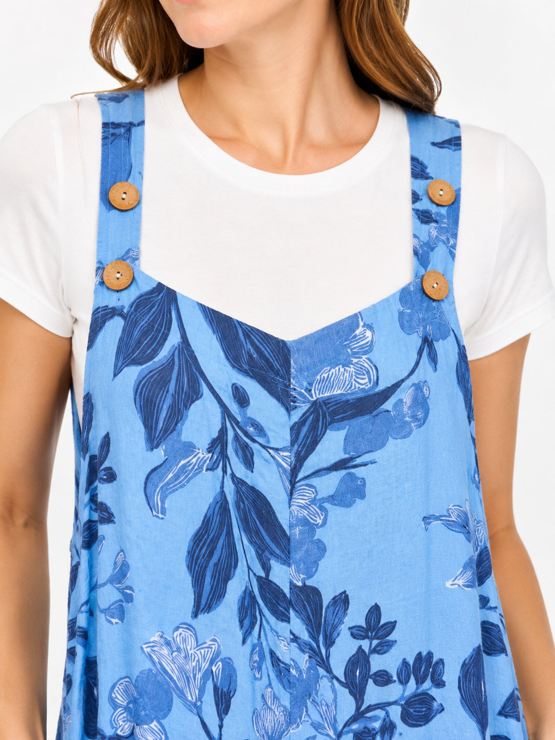 Blue floral patterned sleeveless dress with wooden buttons over white short-sleeve shirt showing neckline and shoulders.