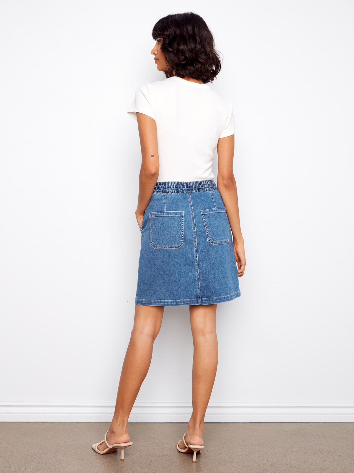 Back view of Charlie B Nautical Tie Waist Denim Skirt in blue denim styled with a white top and neutral heels by Charlie B