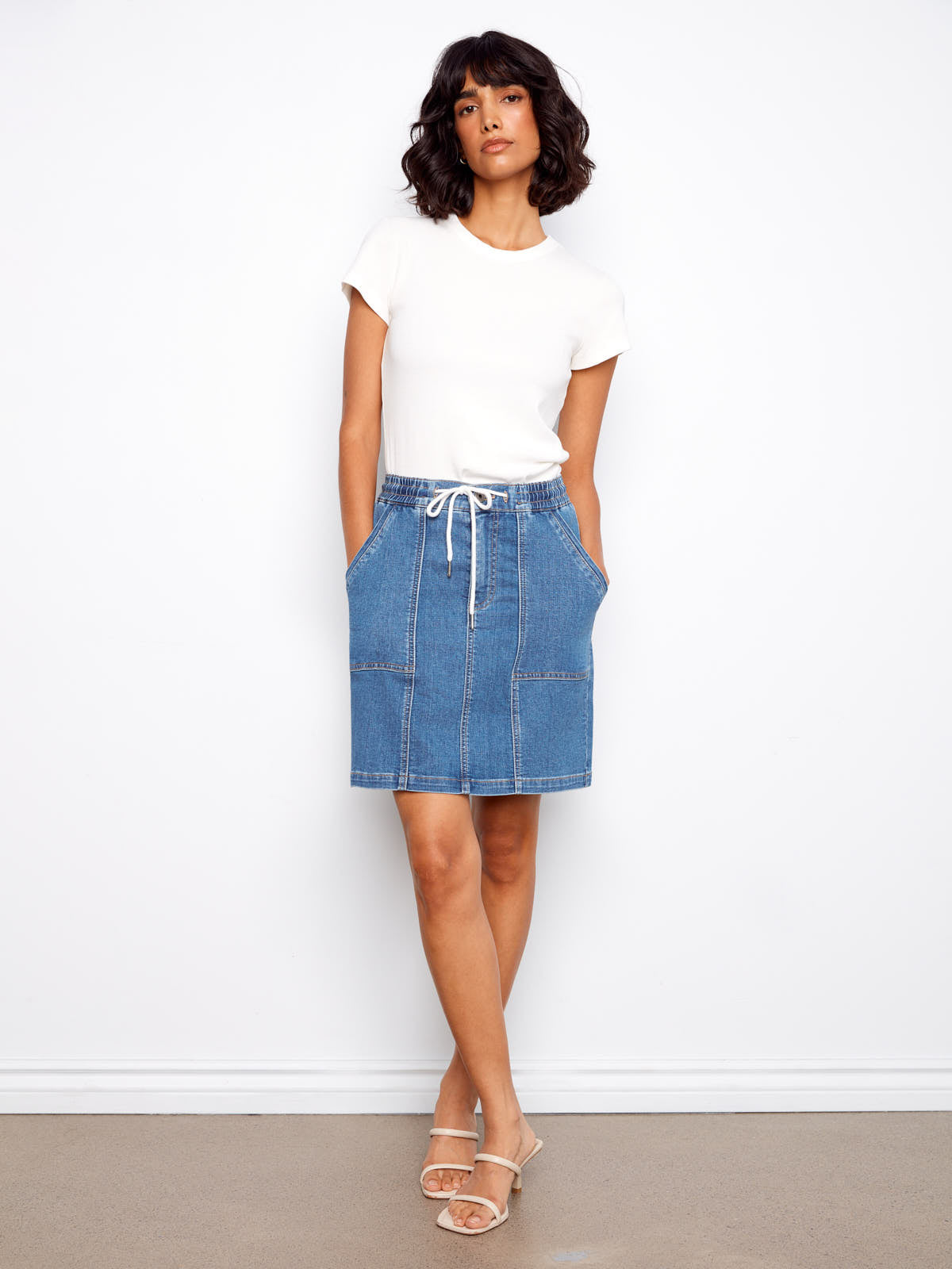 Model wearing a white top with a Charlie B Nautical Tie Waist Denim Skirt in blue denim and sandals