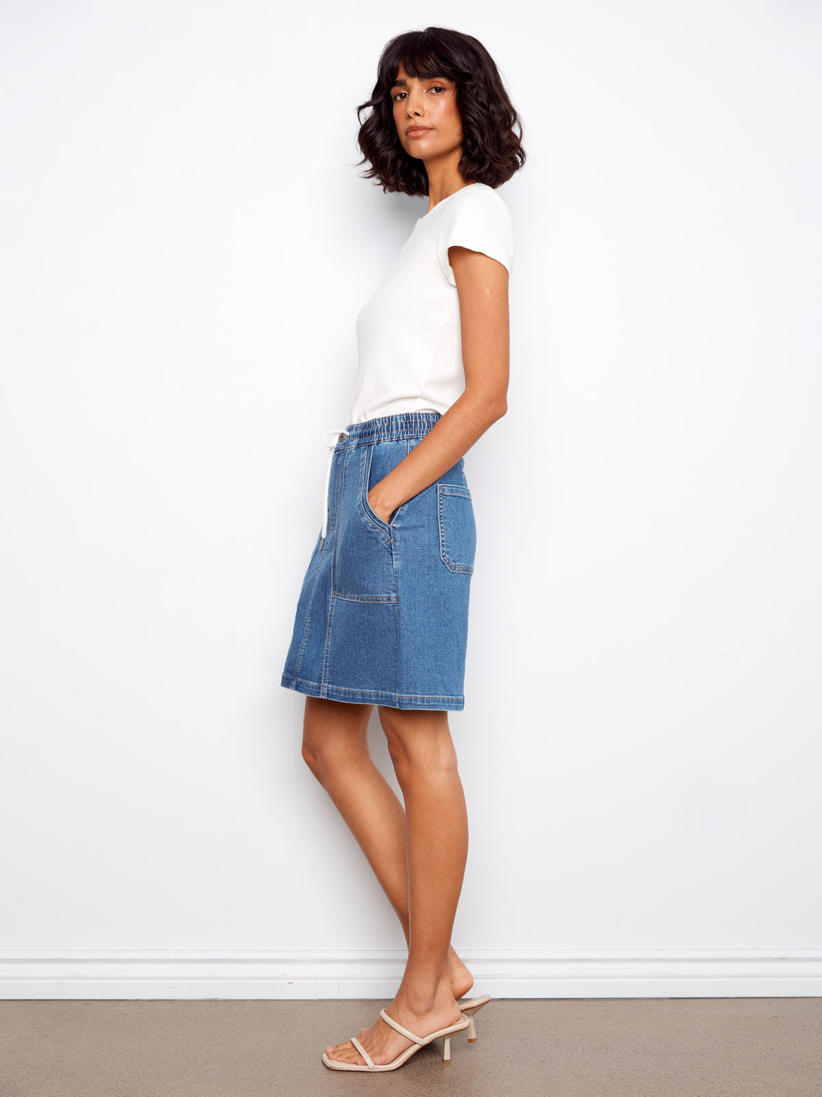 Slim model in white top wearing Charlie B Nautical Tie Waist Denim Skirt by Charlie B in blue denim with pockets
