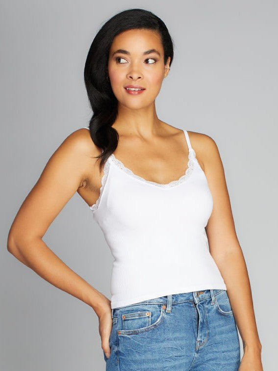 Model in white Lace Trim Bamboo Camisole by Coast To Coast Trading paired with blue denim jeans against gray background