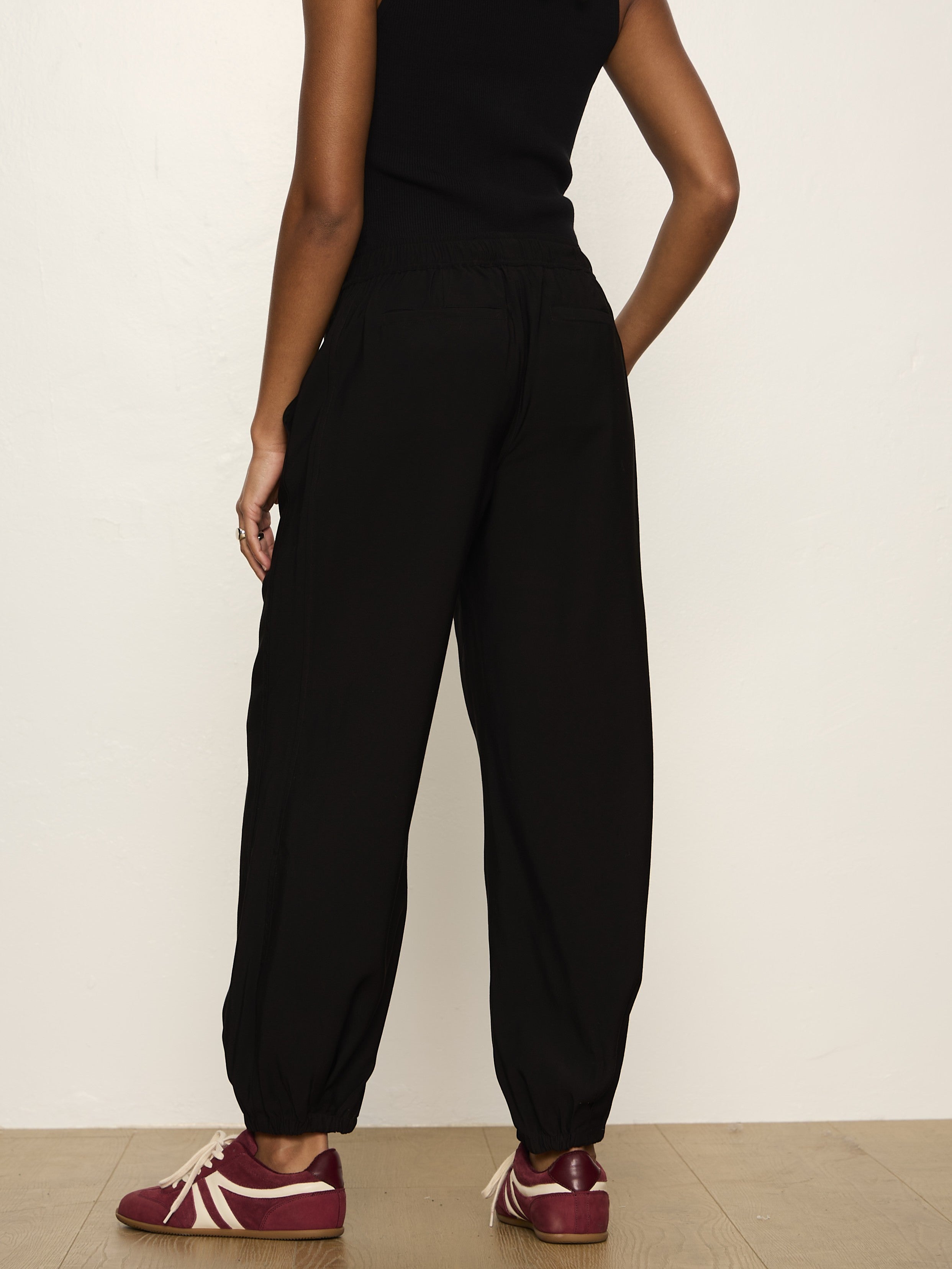 Rear view of a person wearing loose black pants with elastic hems and maroon sneakers with white accents.