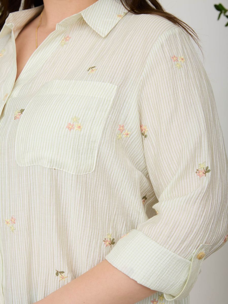 Close-up of a light beige striped shirt with small floral embroidery and a front patch pocket on the chest.