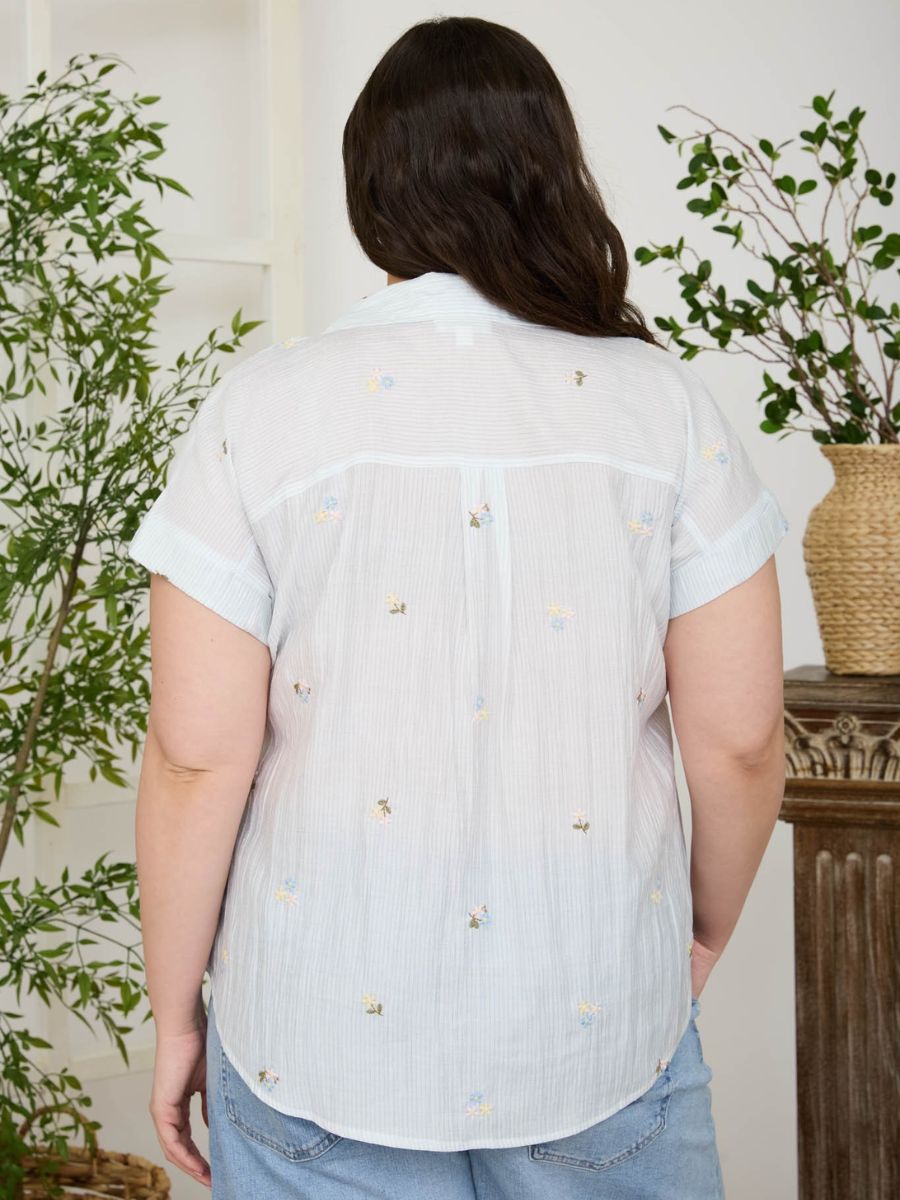 Light blue short-sleeve shirt with small floral embroidery detail on back paired with light denim bottoms.