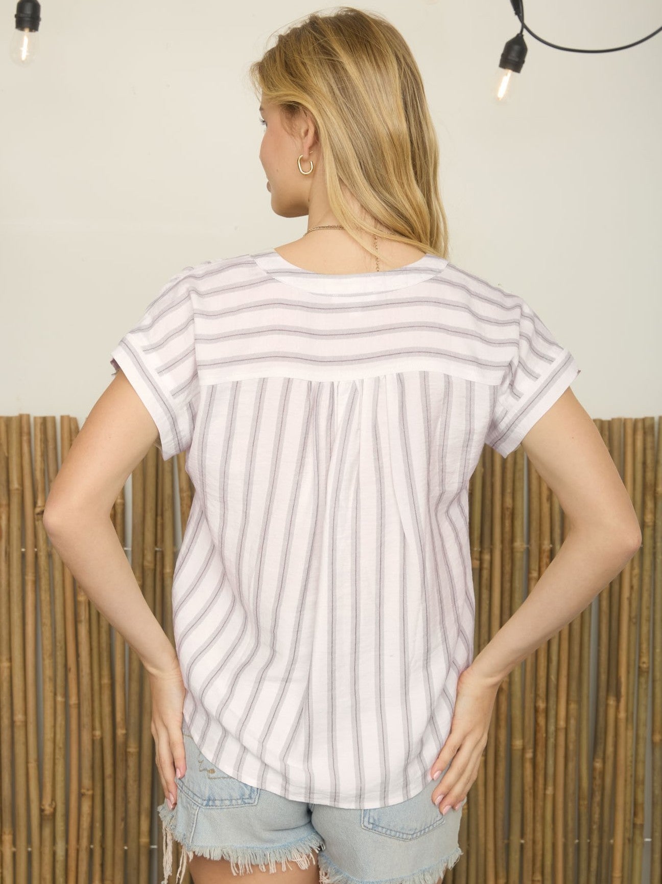 White short-sleeve top with gray vertical and horizontal stripes paired with light denim frayed shorts seen from the back.