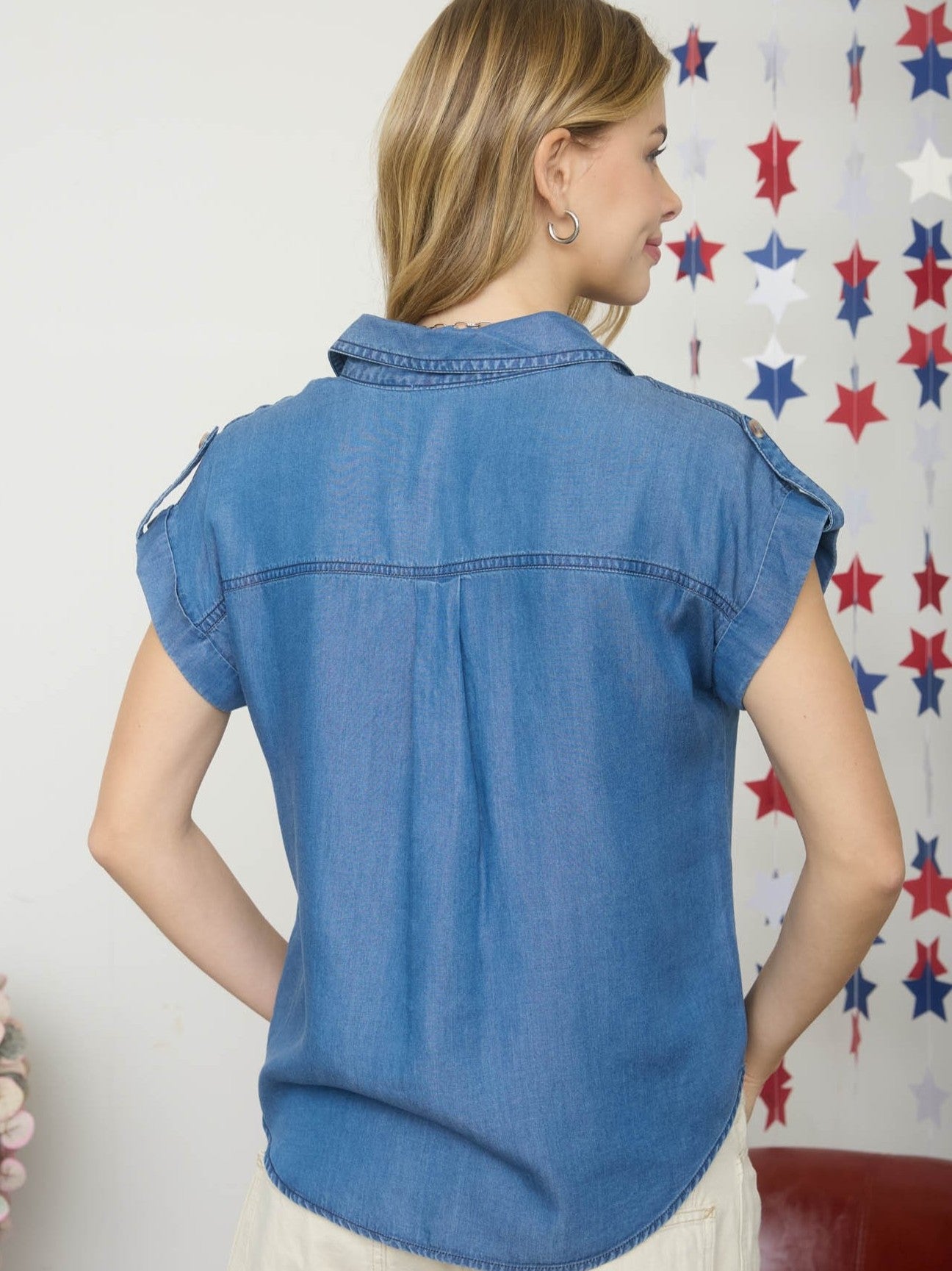 Back view of a short-sleeve denim jacket with shoulder epaulets and rolled cuffs against a star-themed background.