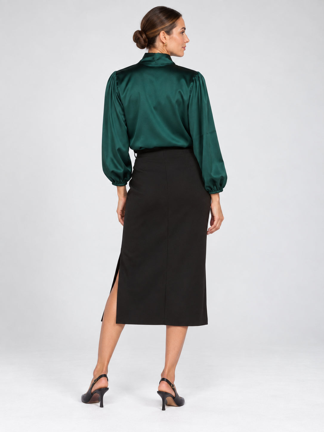 Back view of a model in a green satin blouse, black midi skirt, and black heels