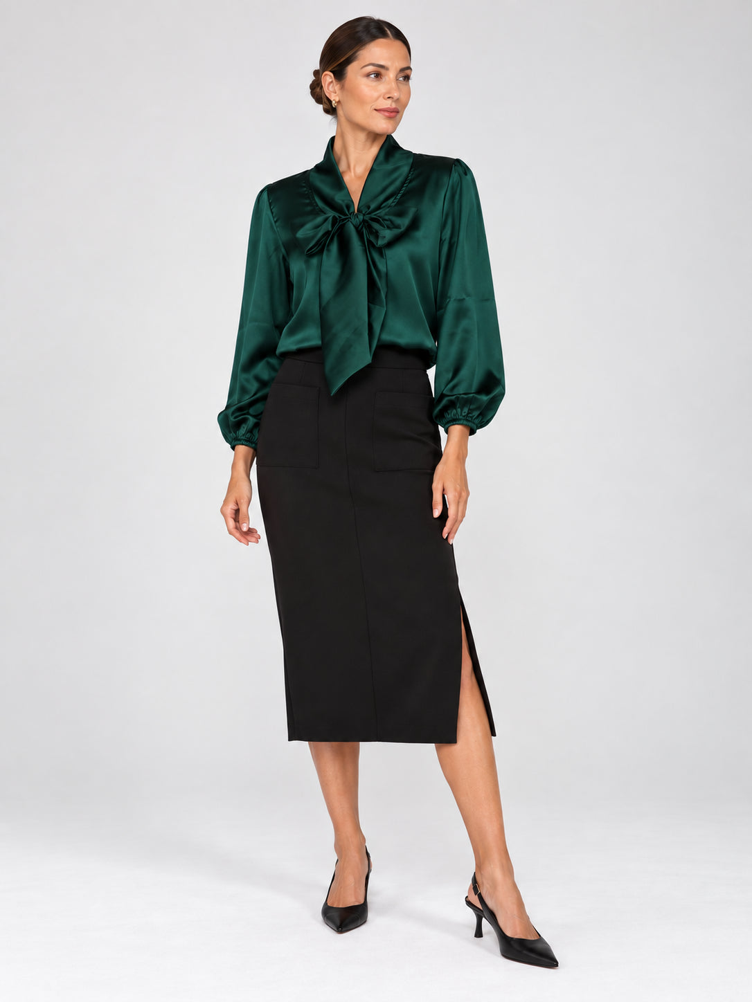 Green satin blouse with a bow neckline and puff sleeves, paired with a black knee-length skirt with side slit