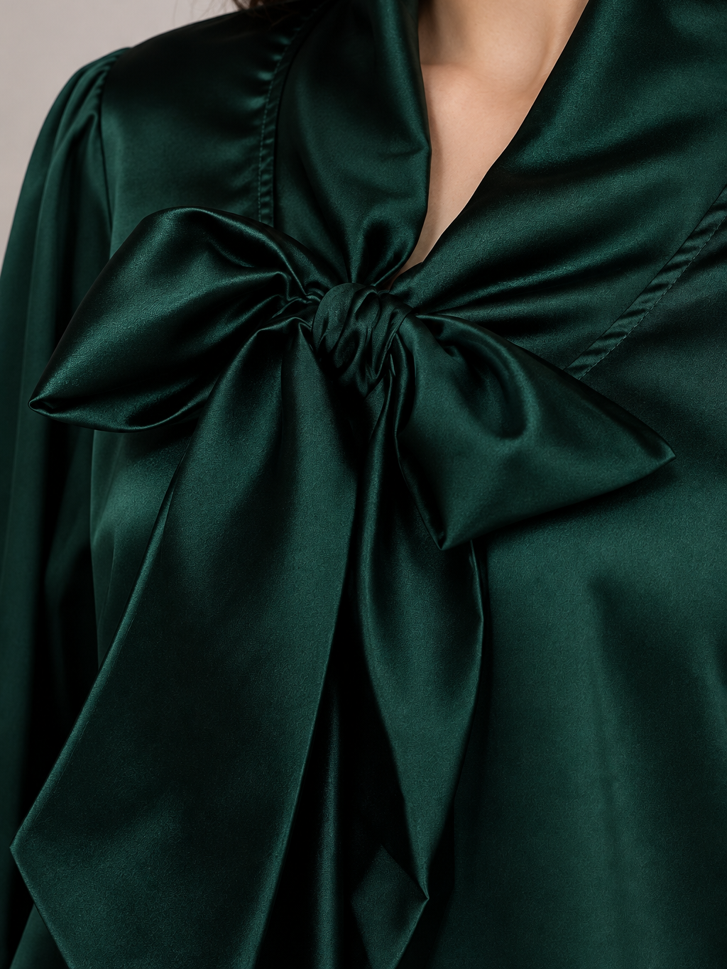 Close-up of a dark green satin top with a large tied bow at the neckline
